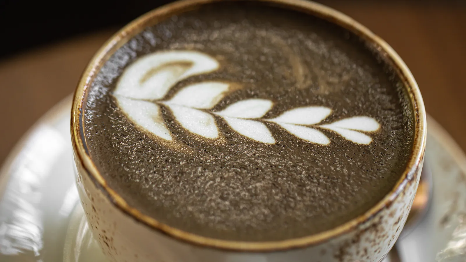 A hojicha latte with leaf latte art in a rustic ceramic cup, seen from above.