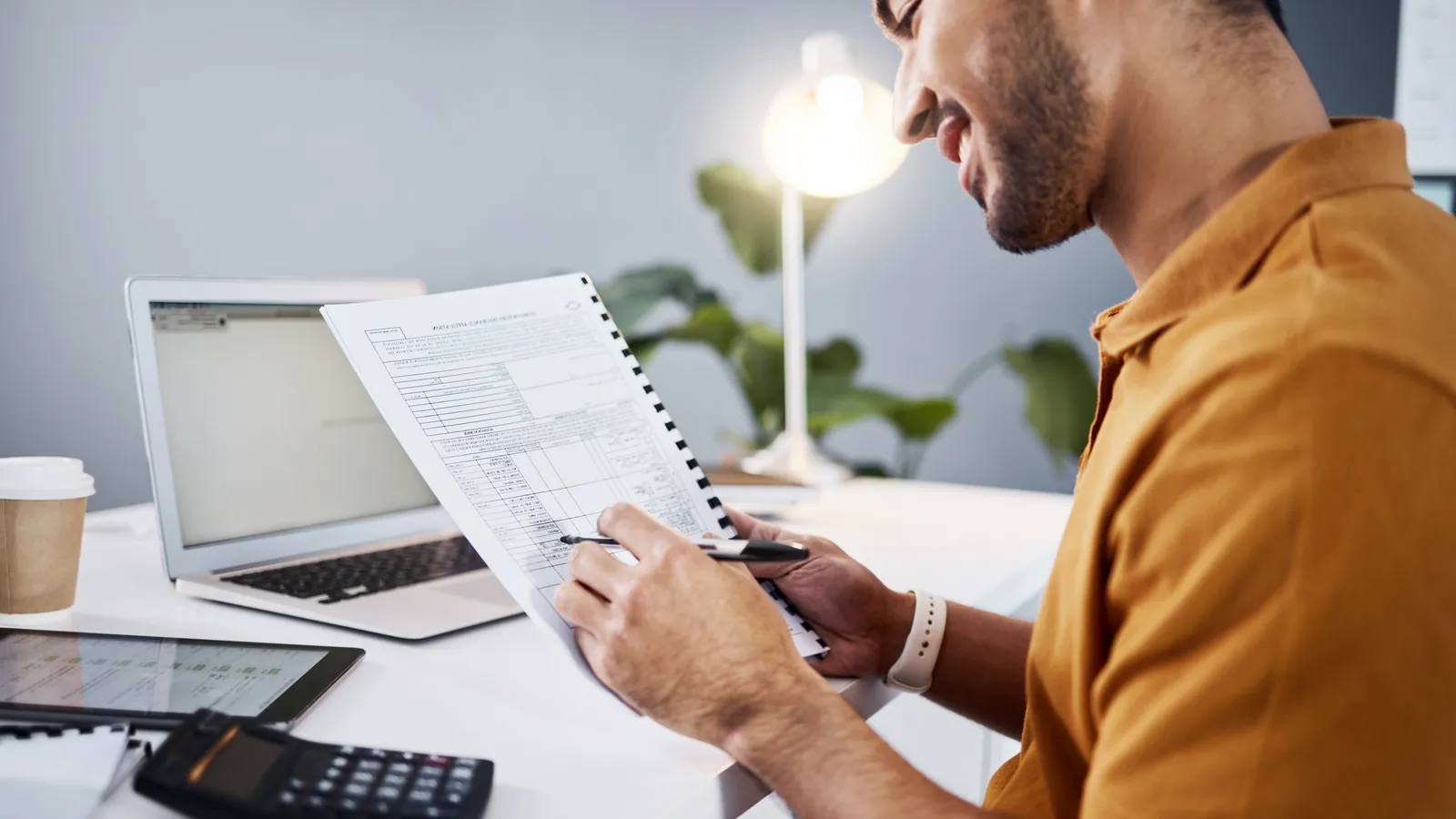 A person reviewing paperwork and figures at a desk with a calculator