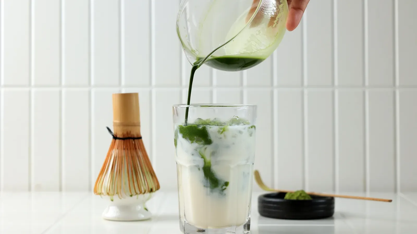 Matcha being poured beside a whisk on a light counter