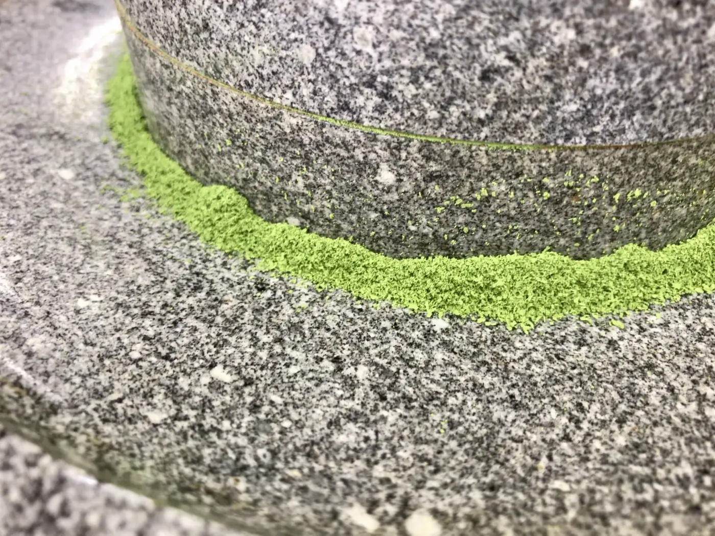 A granite stone mill grinding tencha into a ring of fine bright green matcha powder