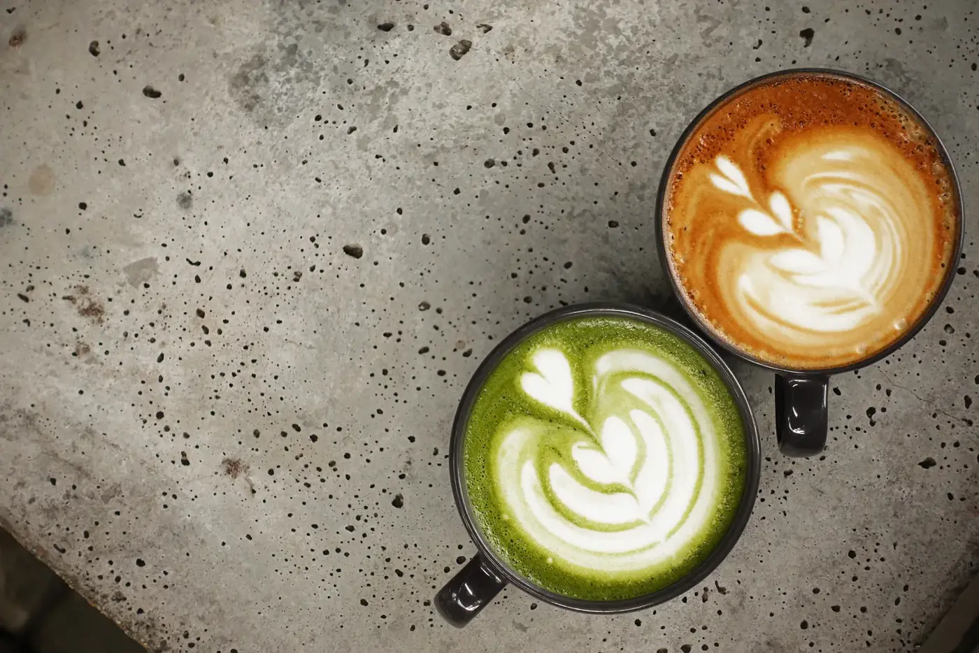 A cup of matcha latte beside a cup of latte art coffee.