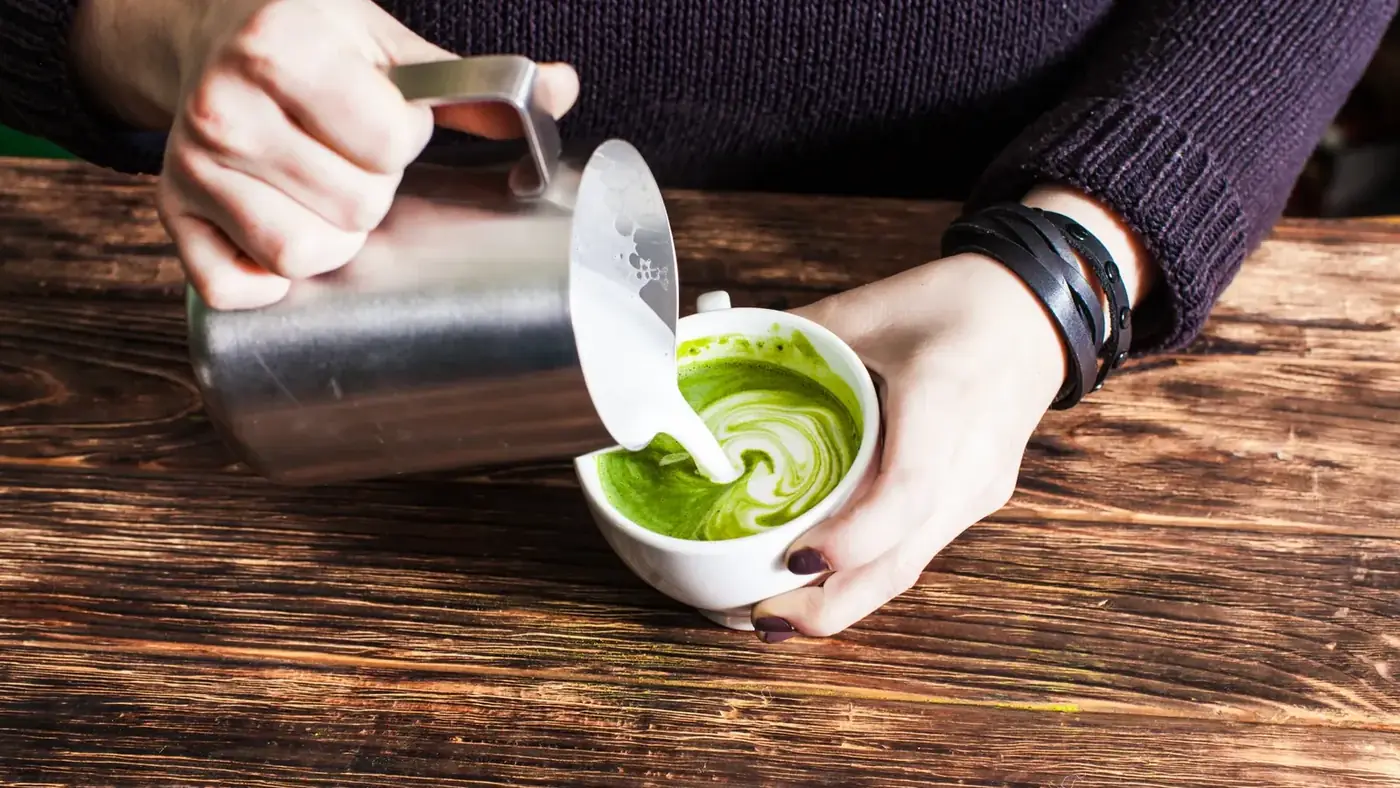 Milk being poured into a cup of whisked matcha