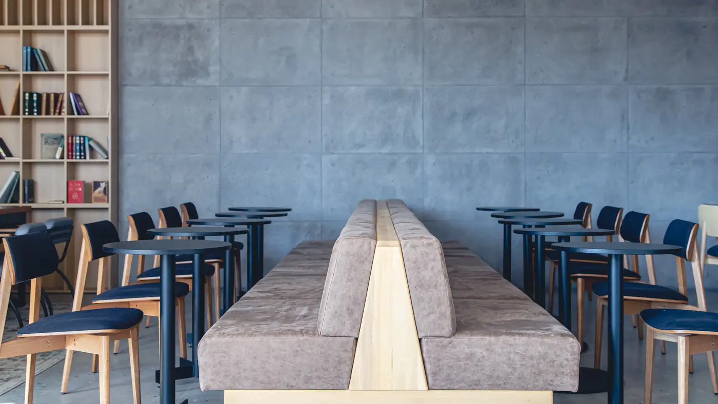 An empty modern cafe with wooden tables, blue chairs and a long upholstered bench before opening.