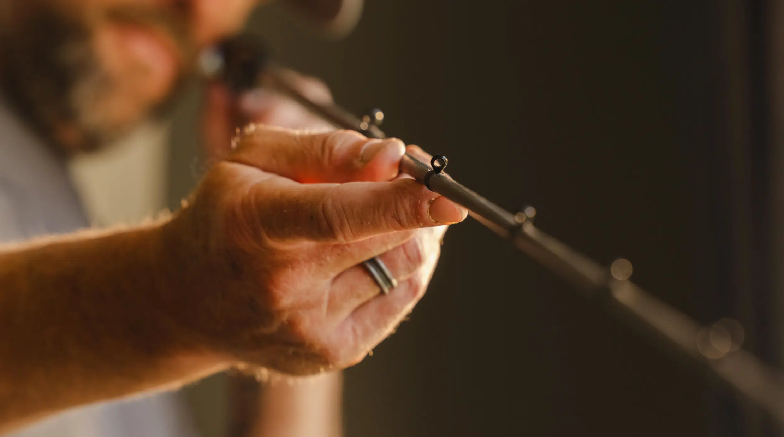 Close-up of a person aiming a fishing rod with a focus on their hand and the rod's eyelet.