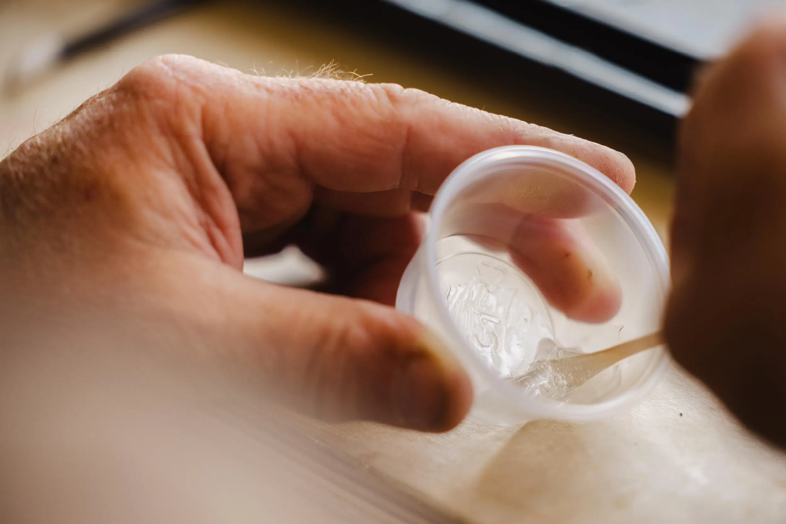 Close-up of a hand holding a small plastic cup while stirring a clear gel inside with a wooden stick.
