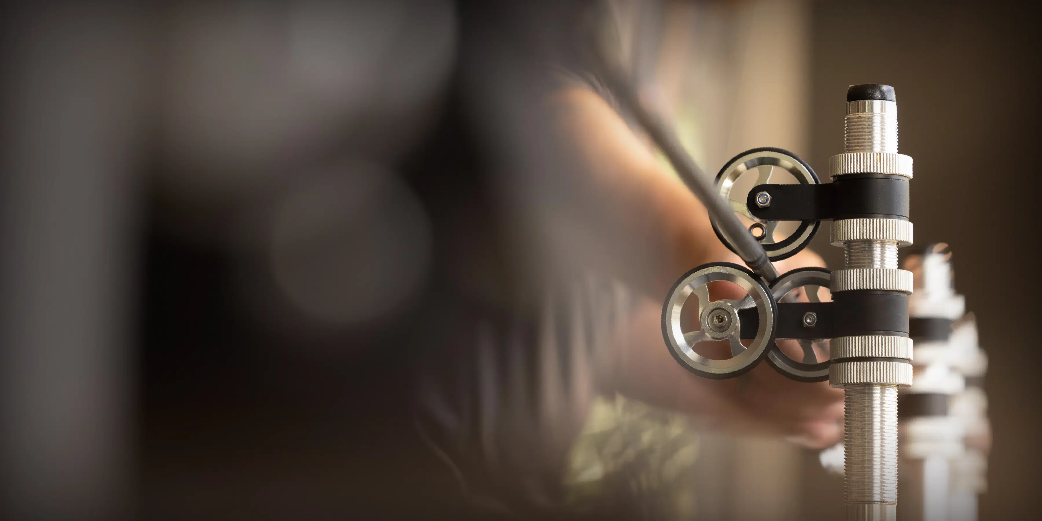 Close-up of a person's hand adjusting a mechanical device with silver wheels and ribbed metallic components.