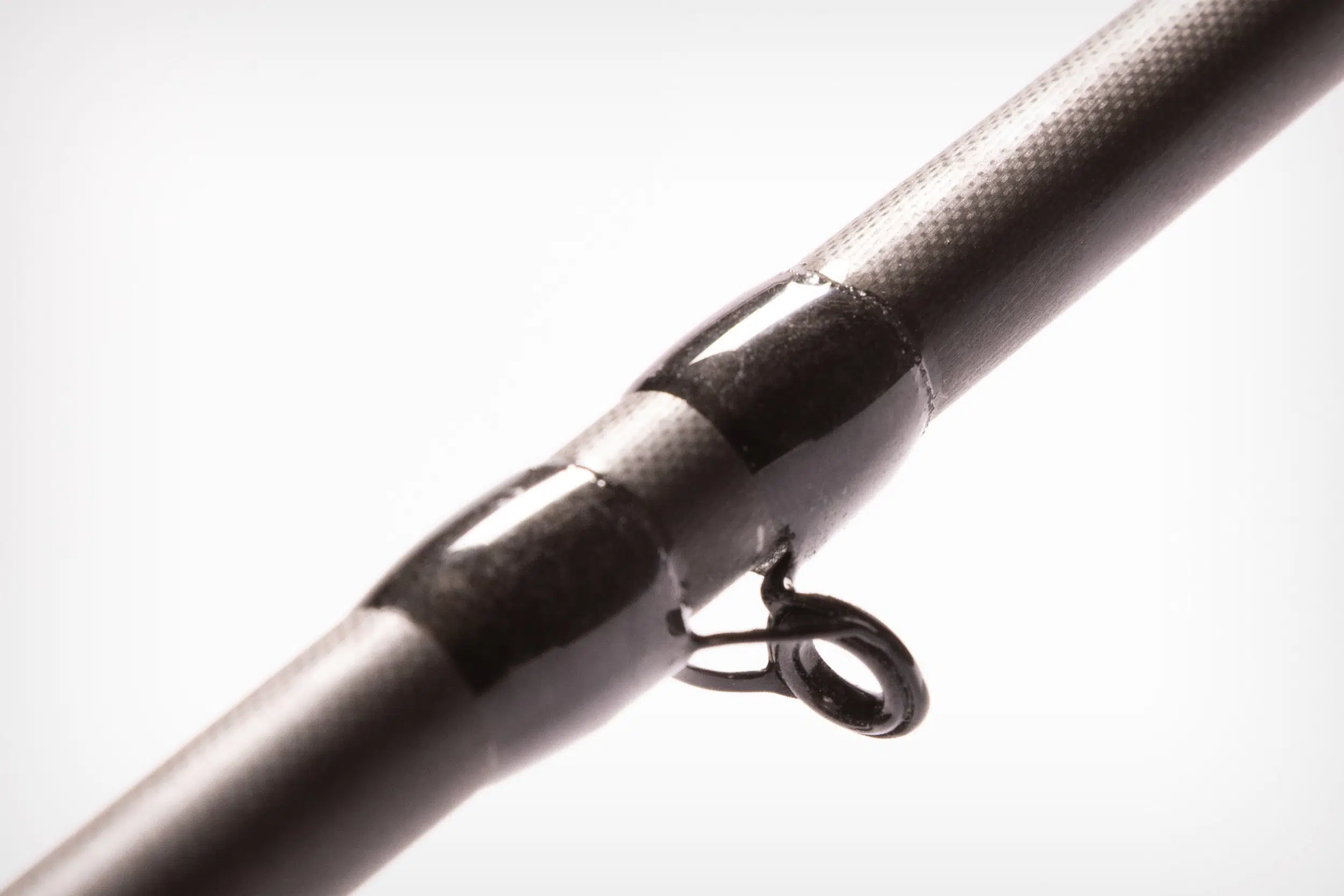 Close-up of a black fishing rod guide on a textured rod surface.