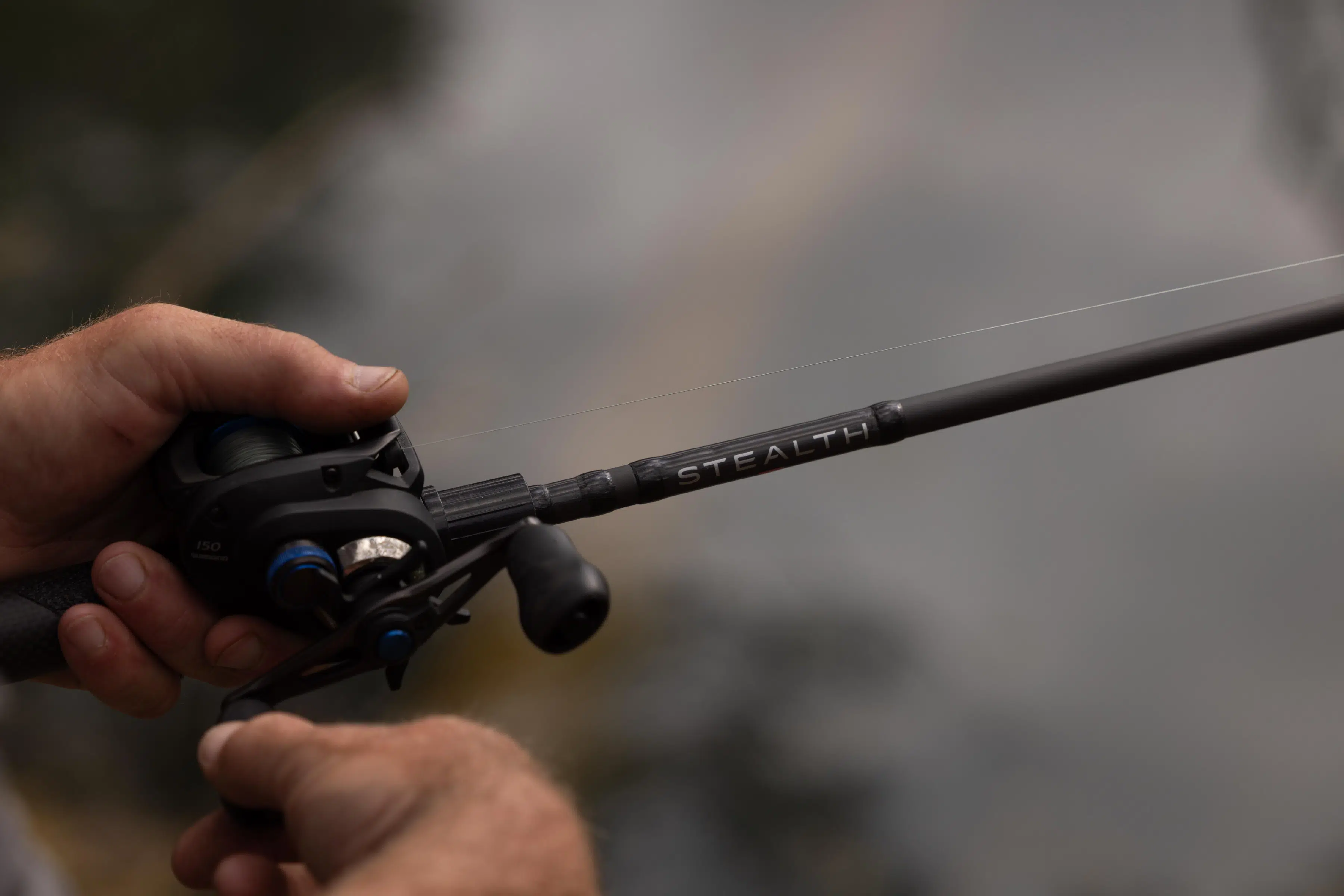 Close-up of hands holding a black fishing rod labeled Stealth with a reel and fishing line.