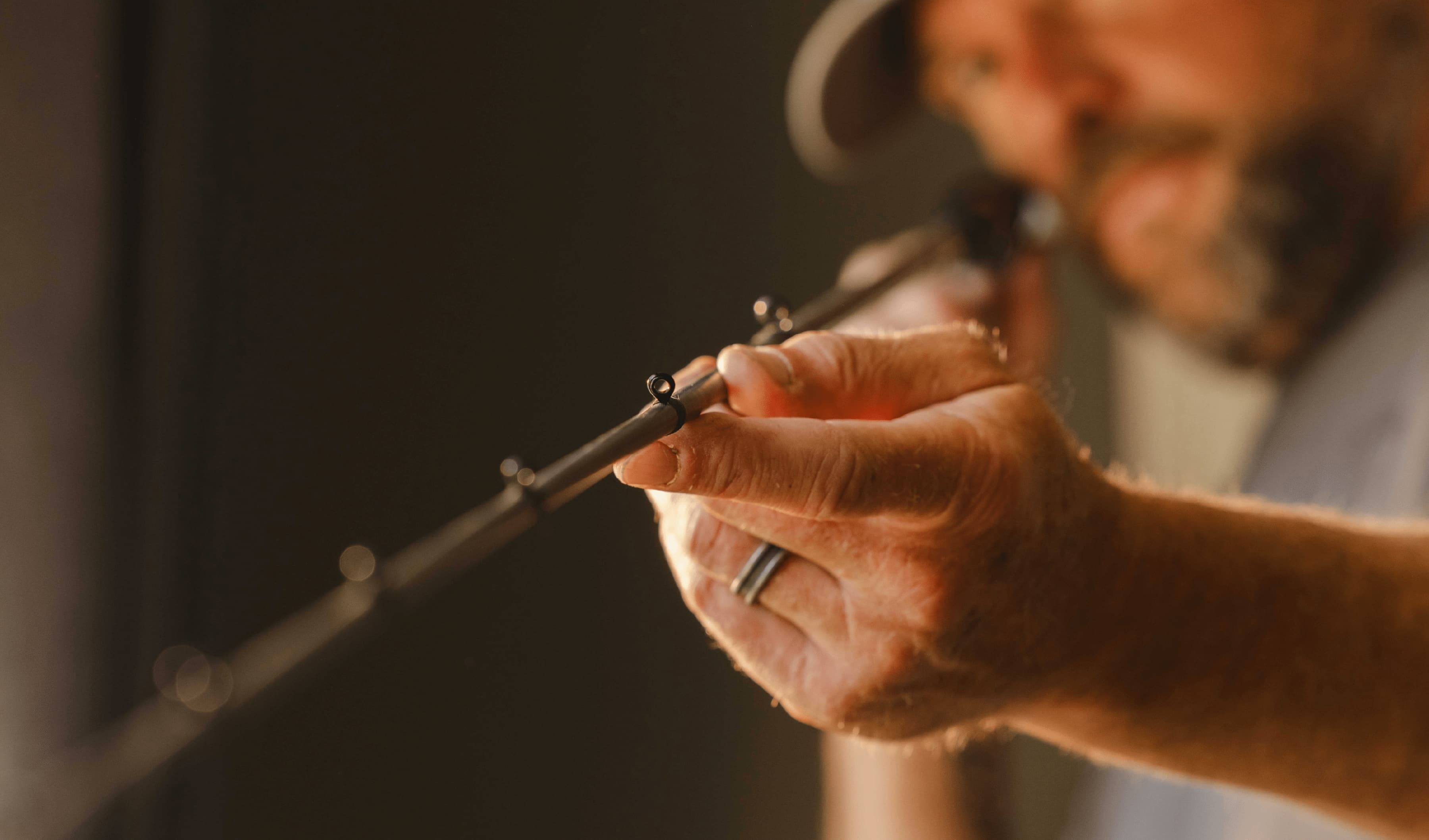 Man wearing a ring carefully tying fishing line to a fishing rod in warm light.