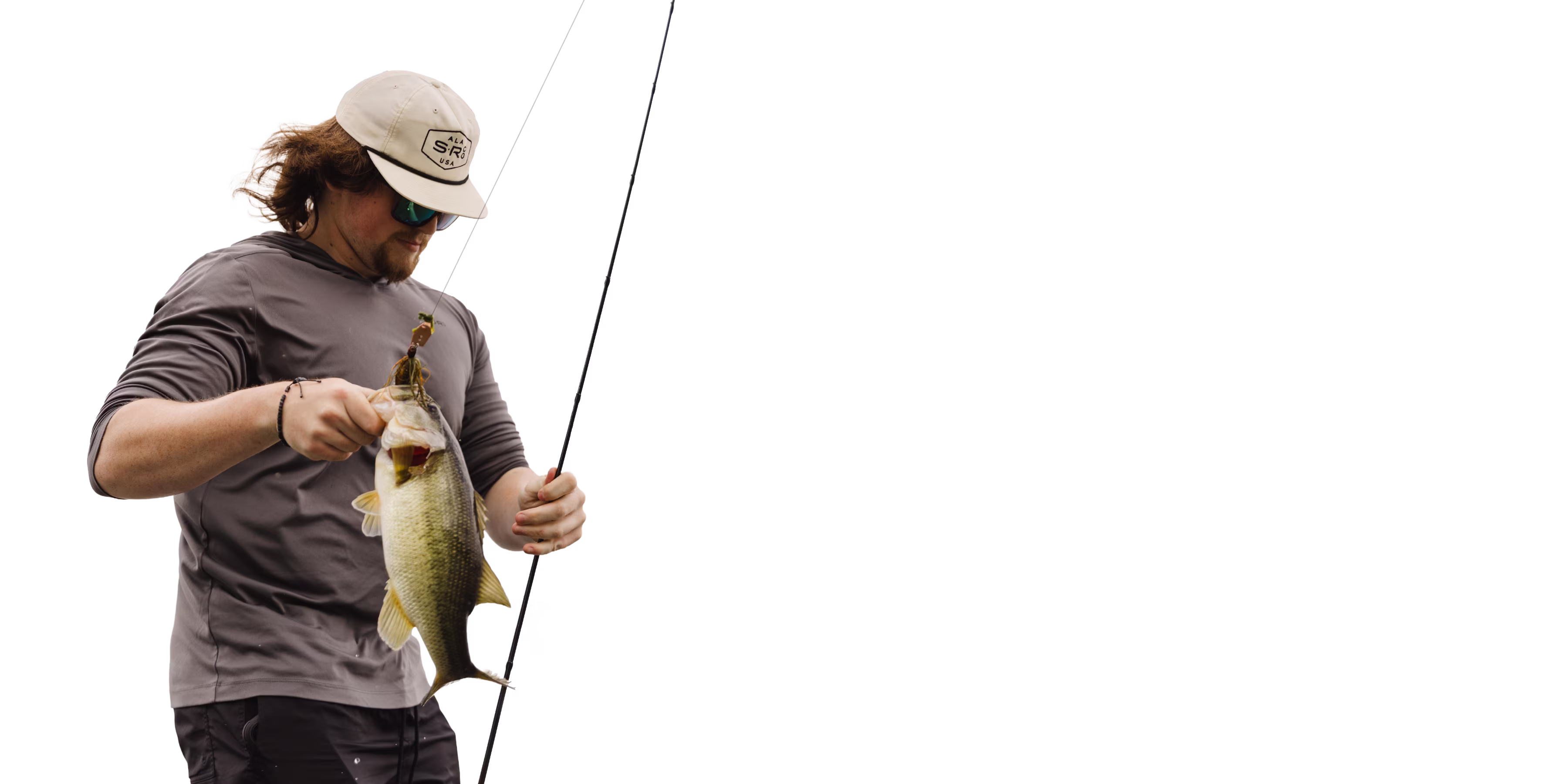 Man wearing cap and sunglasses holding a largemouth bass fish and fishing rod.