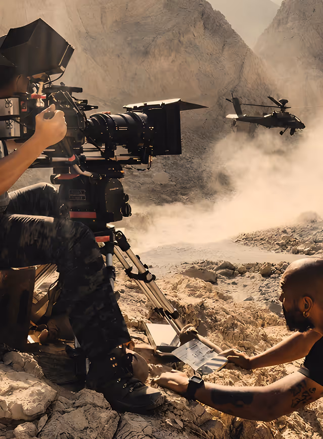 Cinematographer filming an action scene with a professional camera amid dust and debris on a dramatic film set
