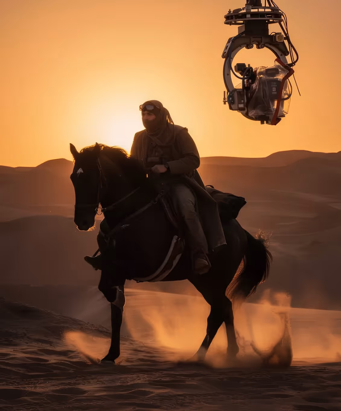 Horseman riding through desert dunes at golden sunset with a film camera crane in the background