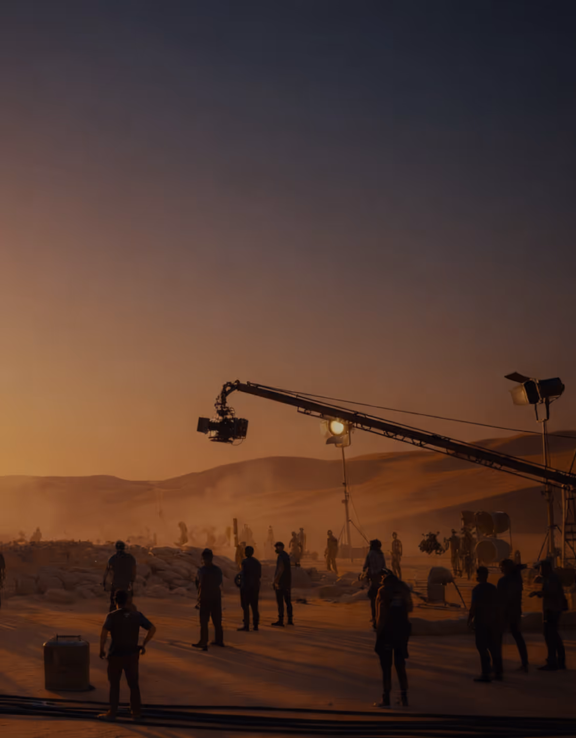 Film crew shooting a scene on a desert location at sunset with a camera crane