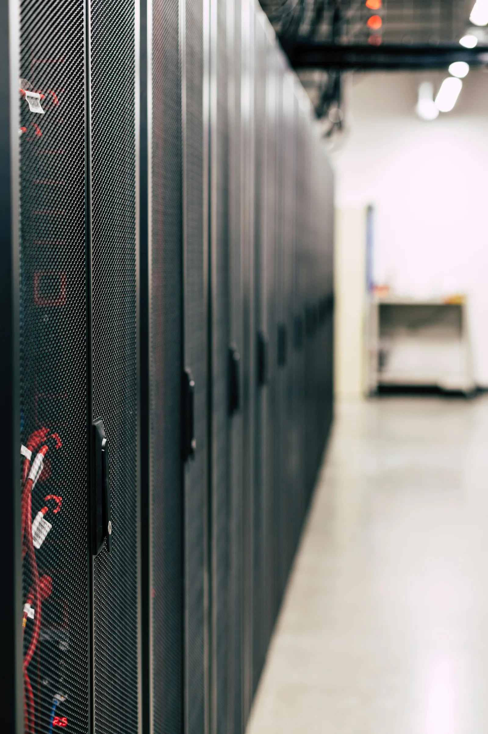 Row of black server racks in a data center with visible red cables inside one rack.