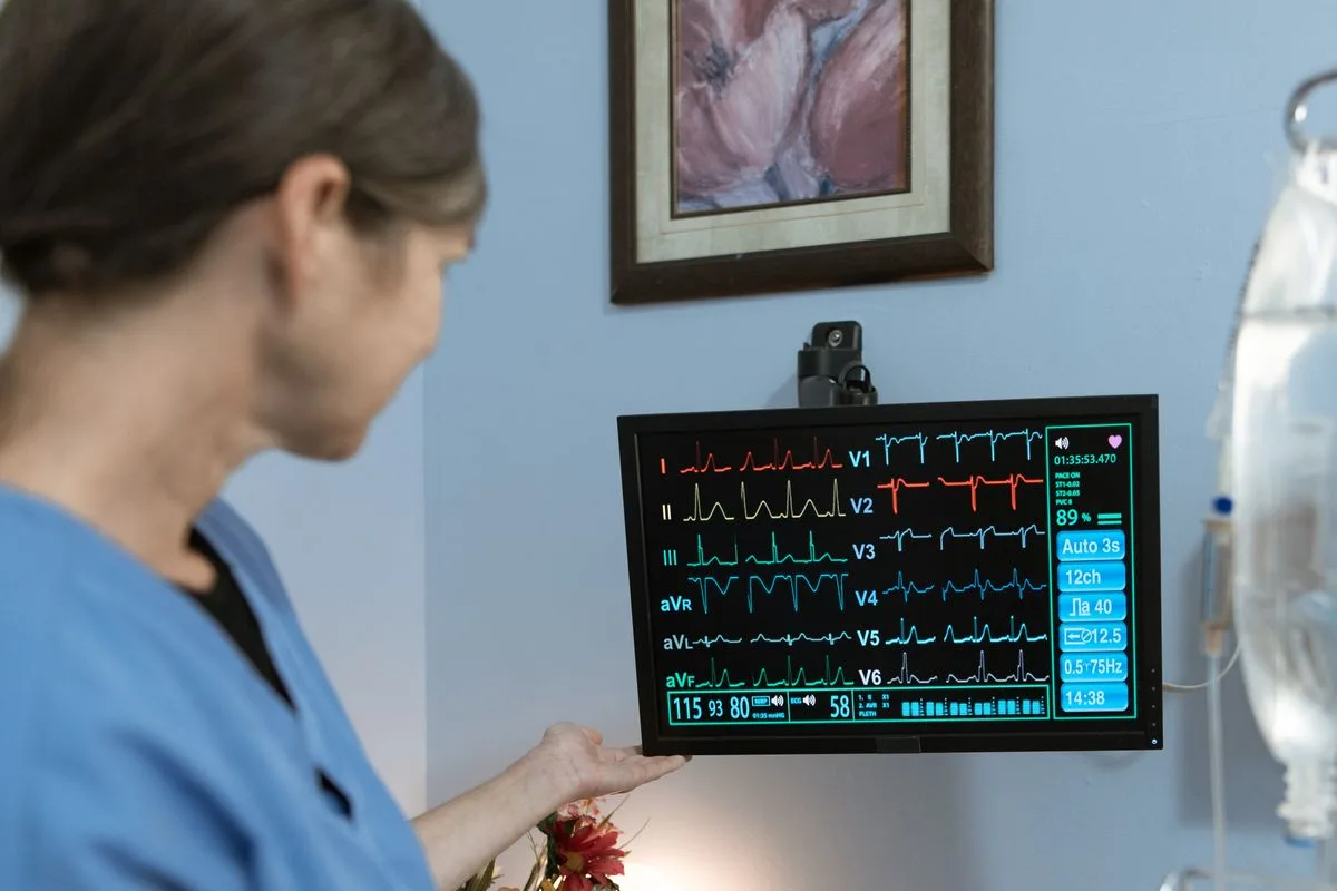 A nurse looking at a patient monitor screen in a clinical room.