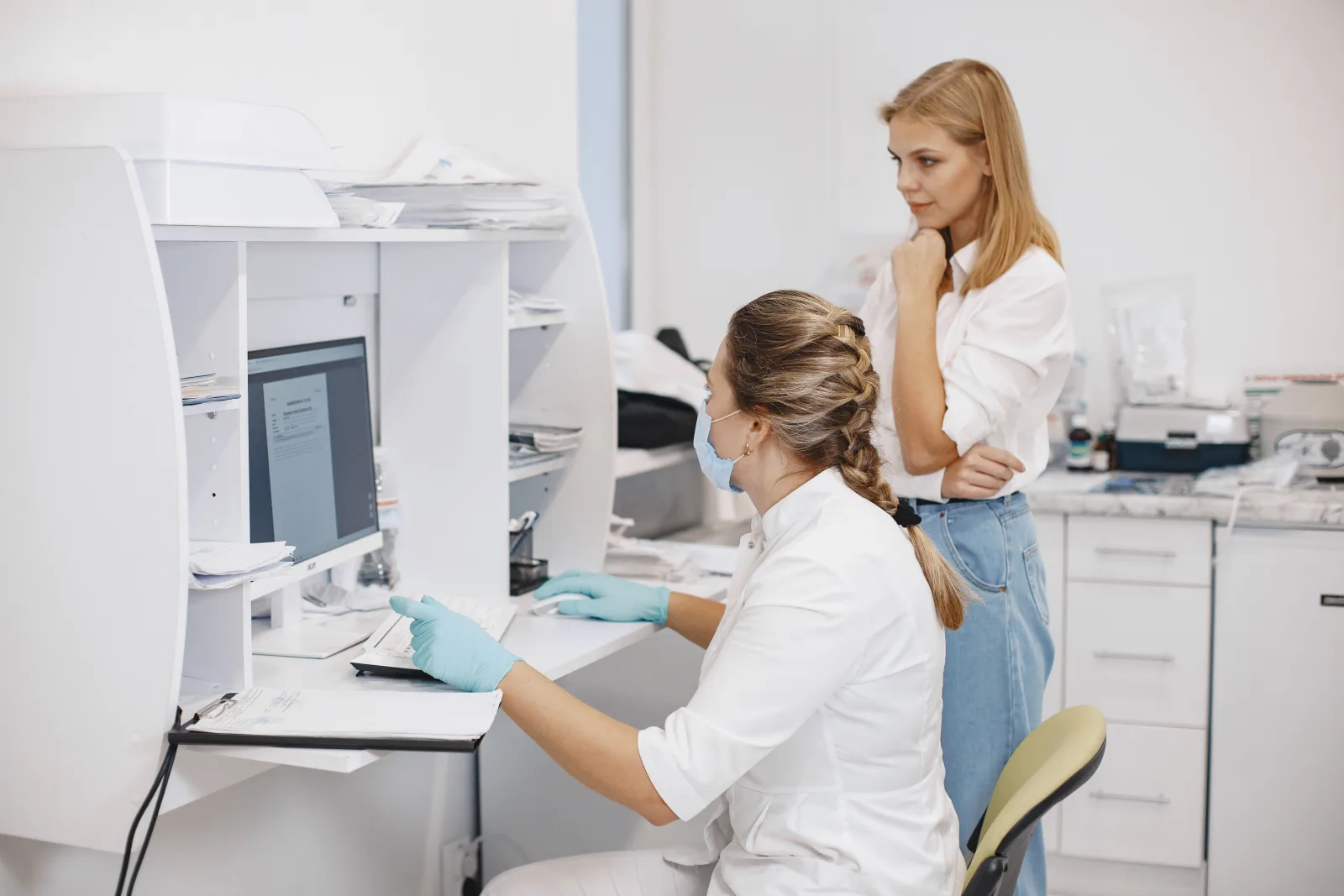 Two healthcare workers reviewing information on a computer in a clinical office.