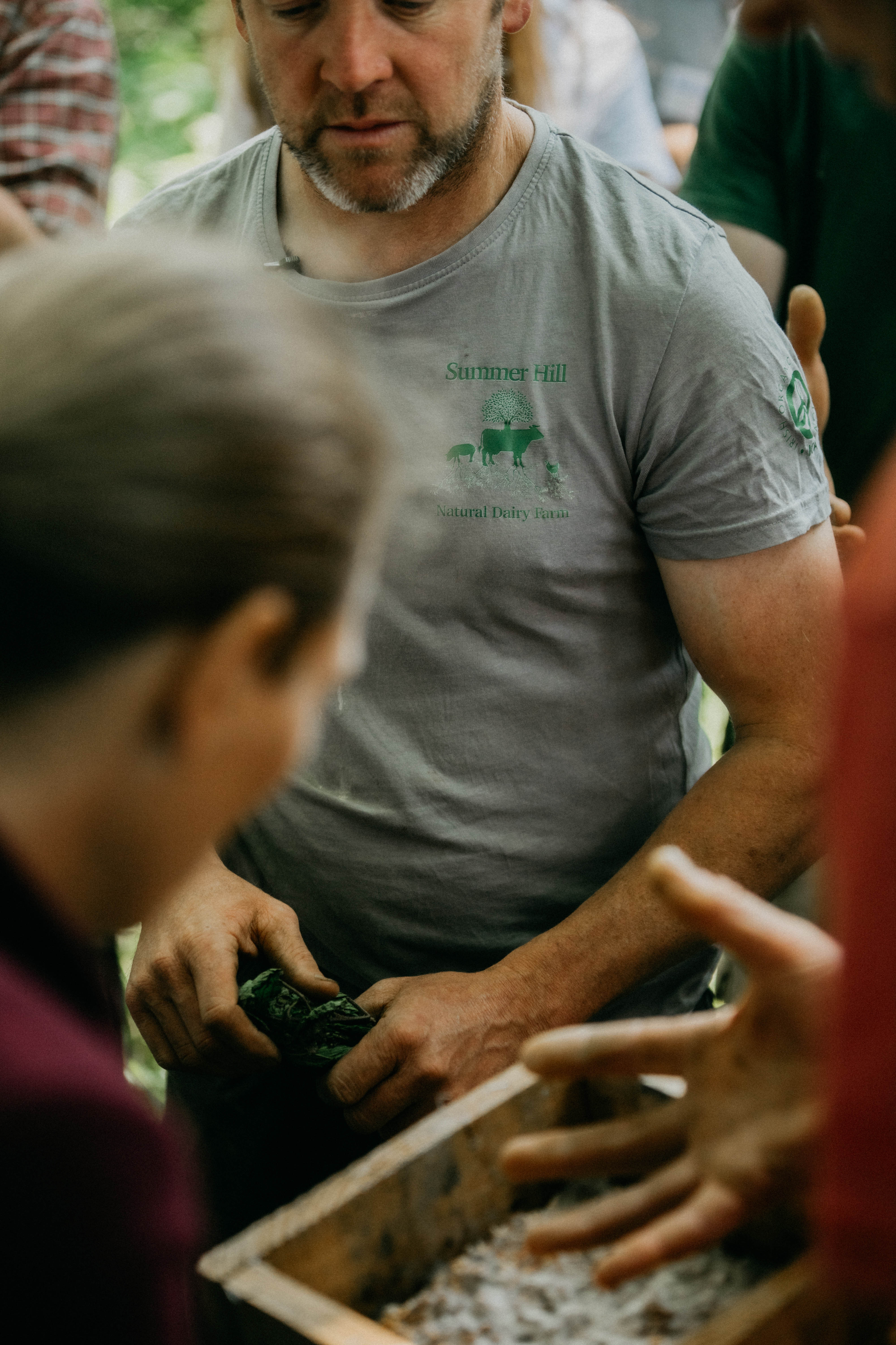 Man in a Summer Hill Natural Dairy Farm shirt holding green leaves among a group of people.