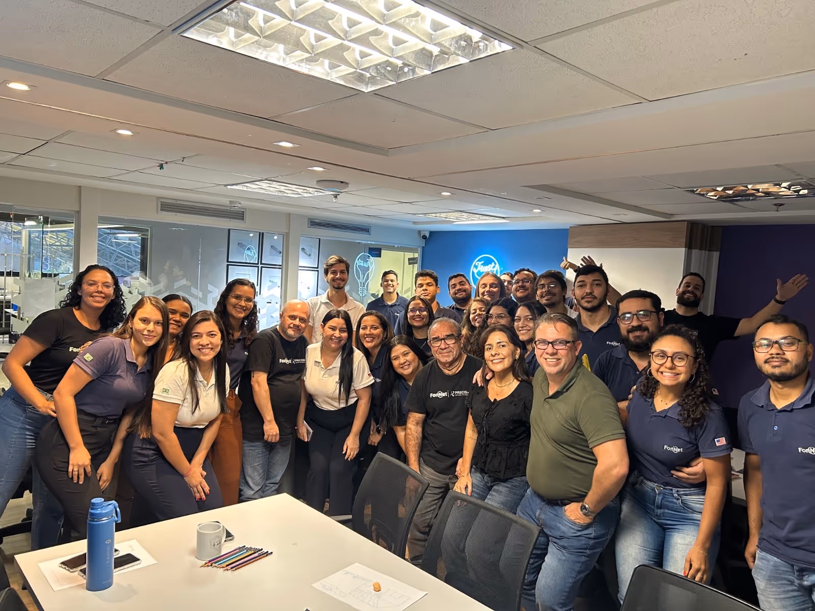 Grupo de pessoas posando pra foto ao redor de uma mesa e sorrindo