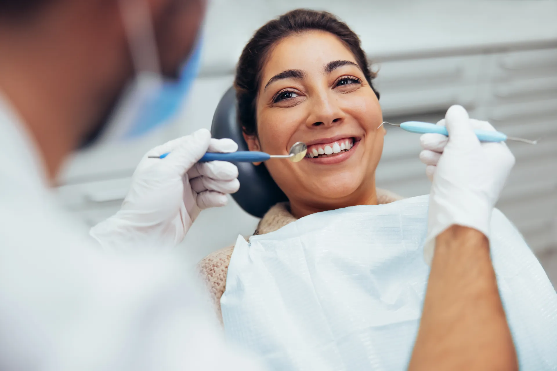 Smiling woman undergoing dental checkup with dentist holding dental tools near her teeth.