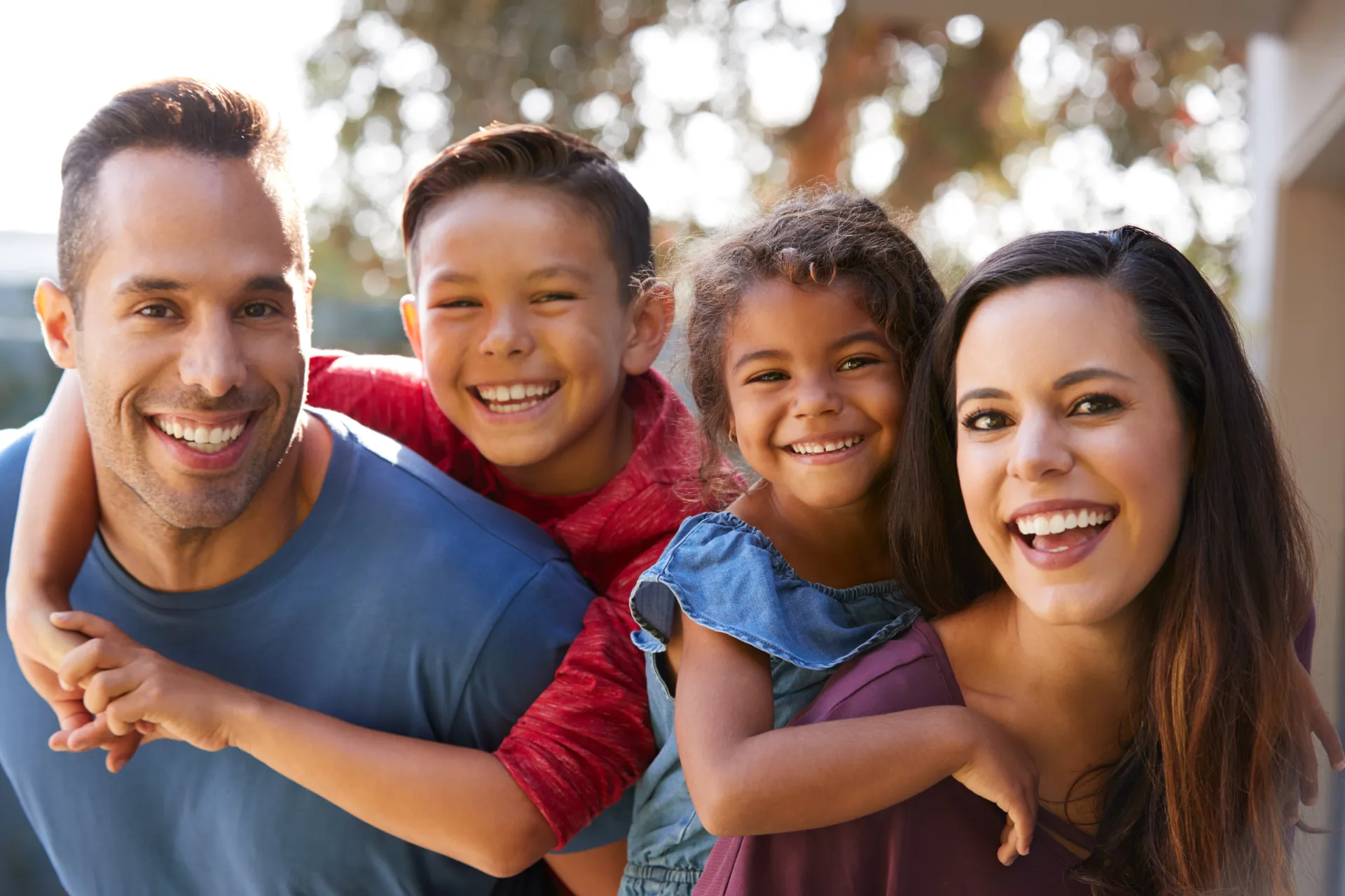 Smiling family with children on parents' backs outdoors in daylight.