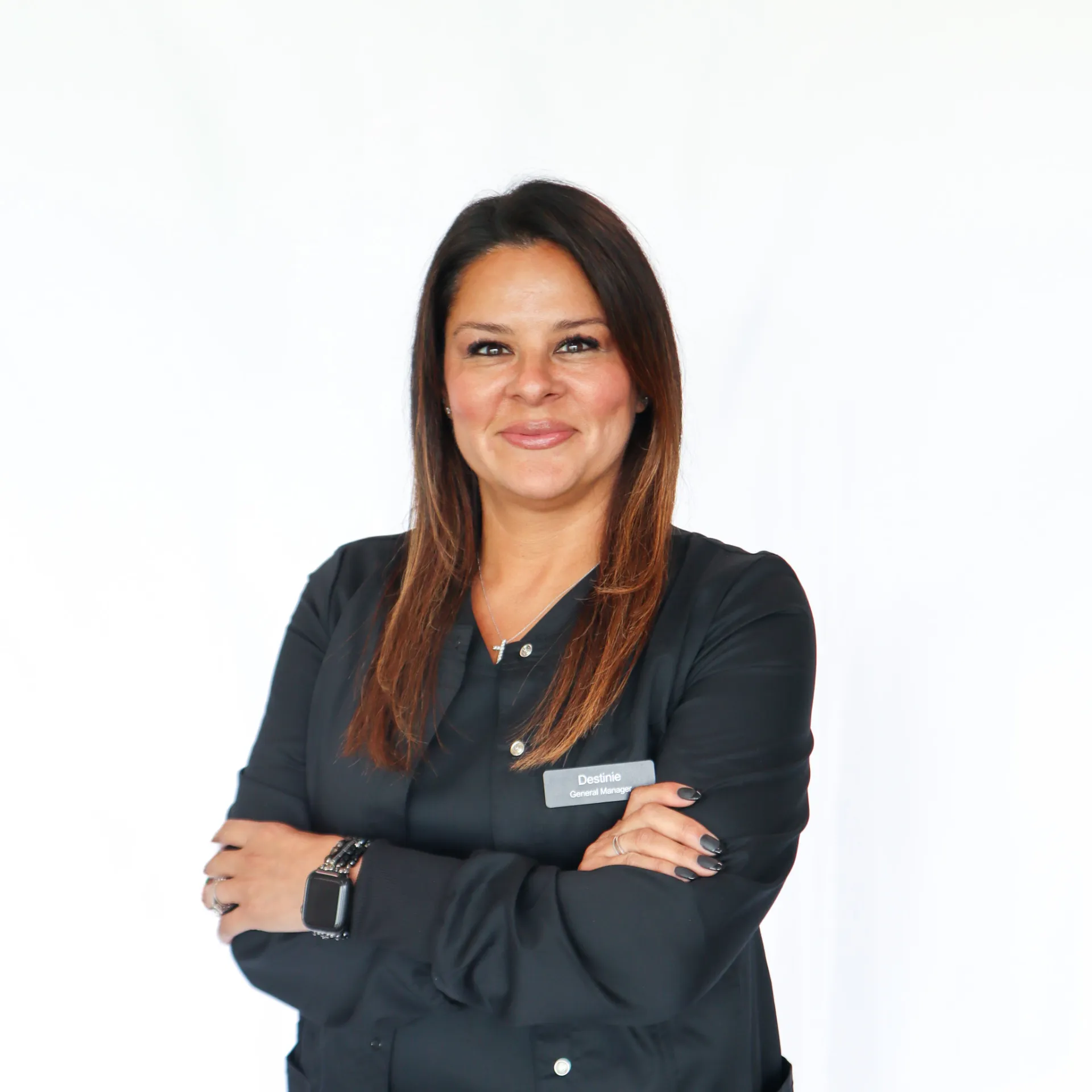 Smiling woman with long brown hair wearing a black shirt and name tag that says Destinie General Manager, standing with arms crossed.