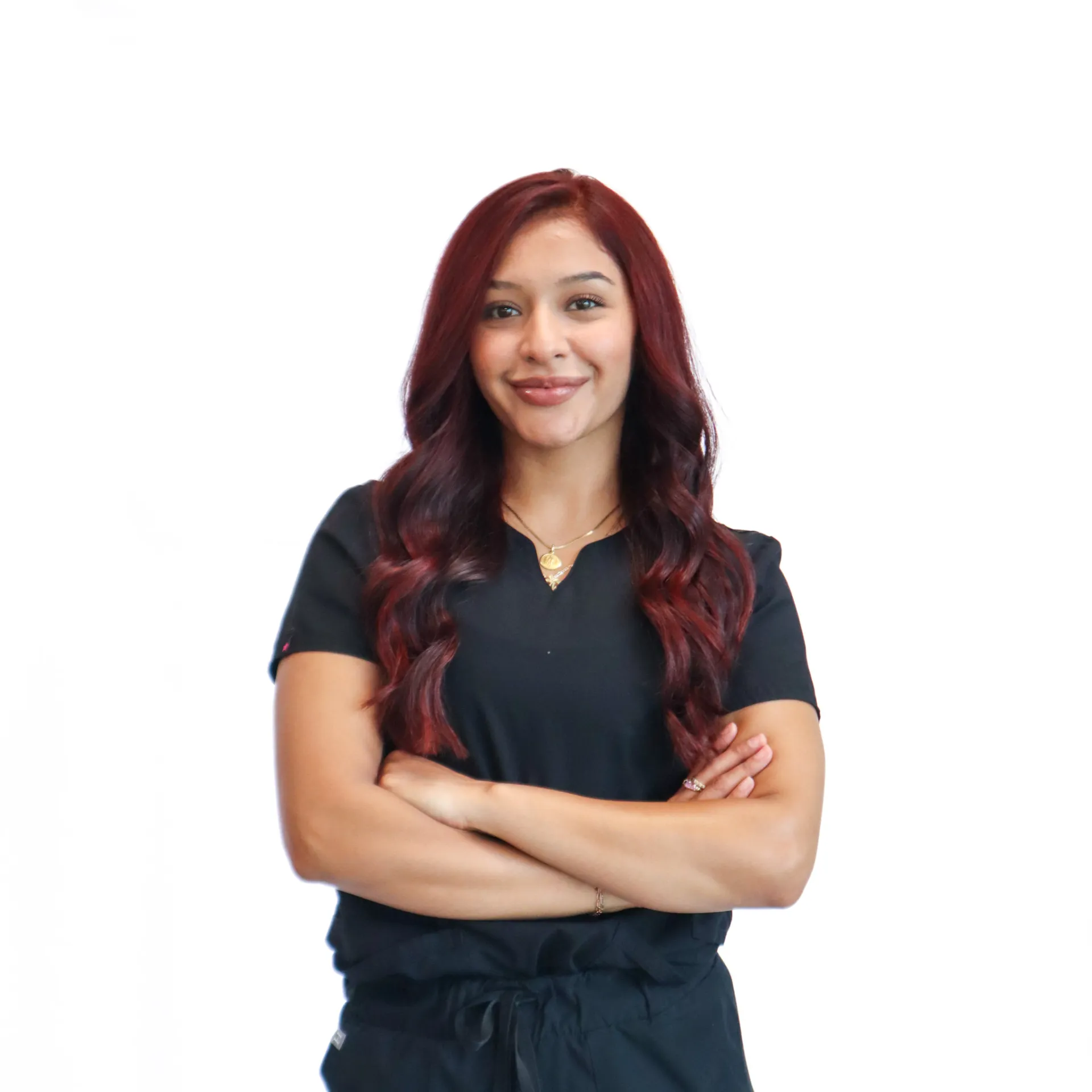 Smiling woman with long red hair wearing black medical scrubs standing with arms crossed.