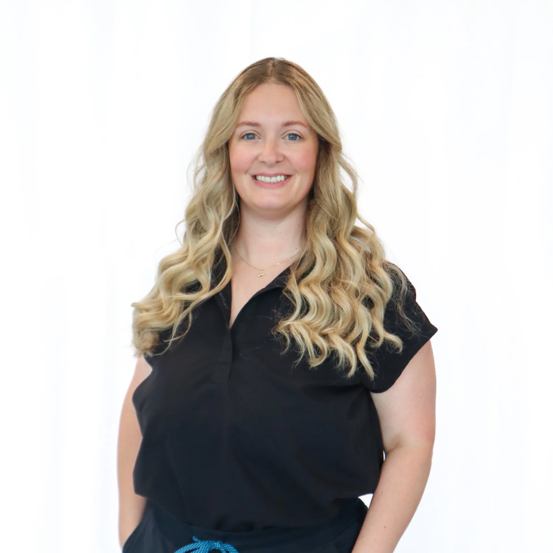 Smiling woman with long wavy blonde hair wearing a black shirt against a white background.