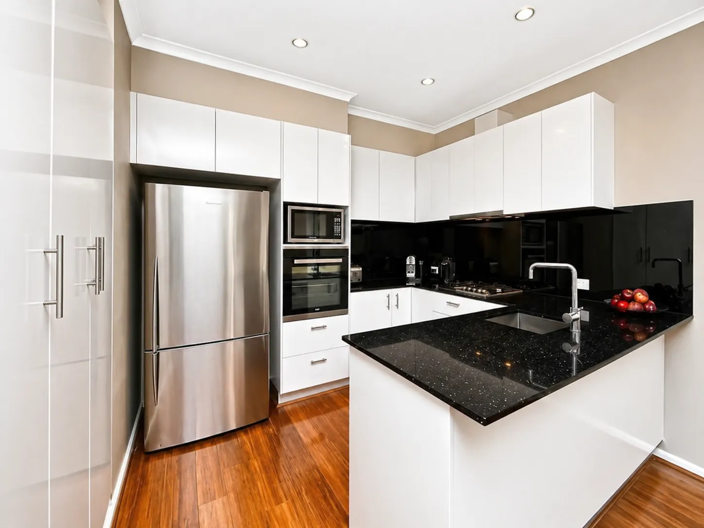 Modern kitchen with white cabinets, black granite countertops, stainless steel refrigerator, built-in microwave and oven, gas stove, and a bowl of red apples.