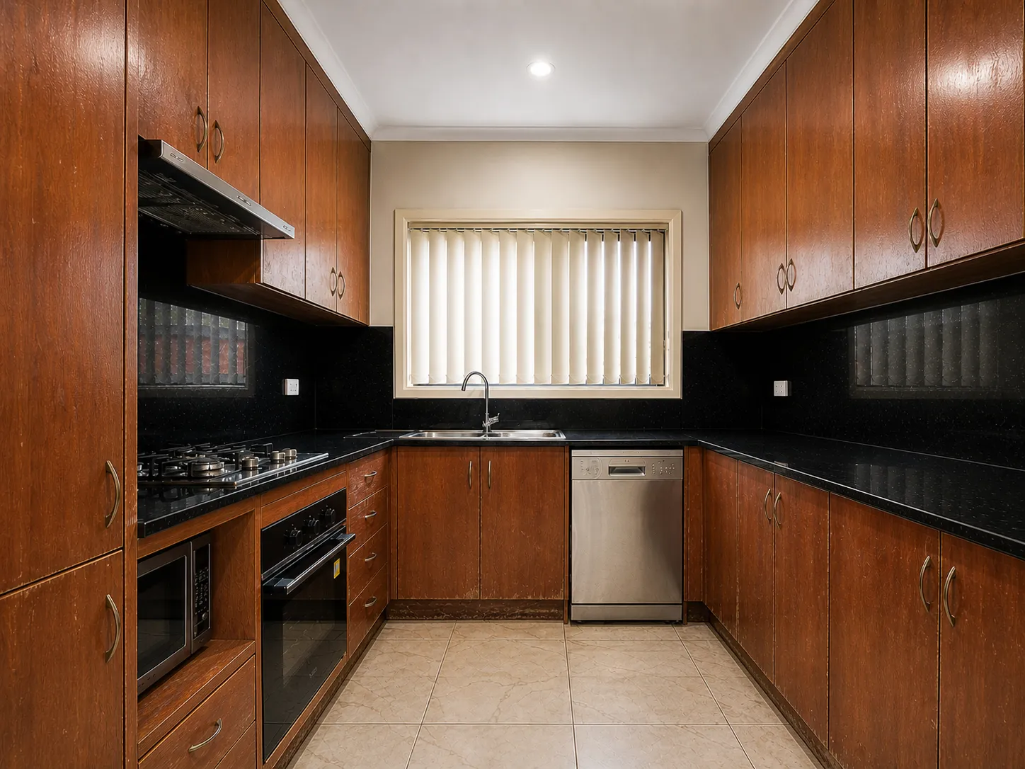 U-shaped kitchen with wooden cabinets, black countertops, tile floor, stainless steel dishwasher, oven, stove, and a window with vertical blinds.