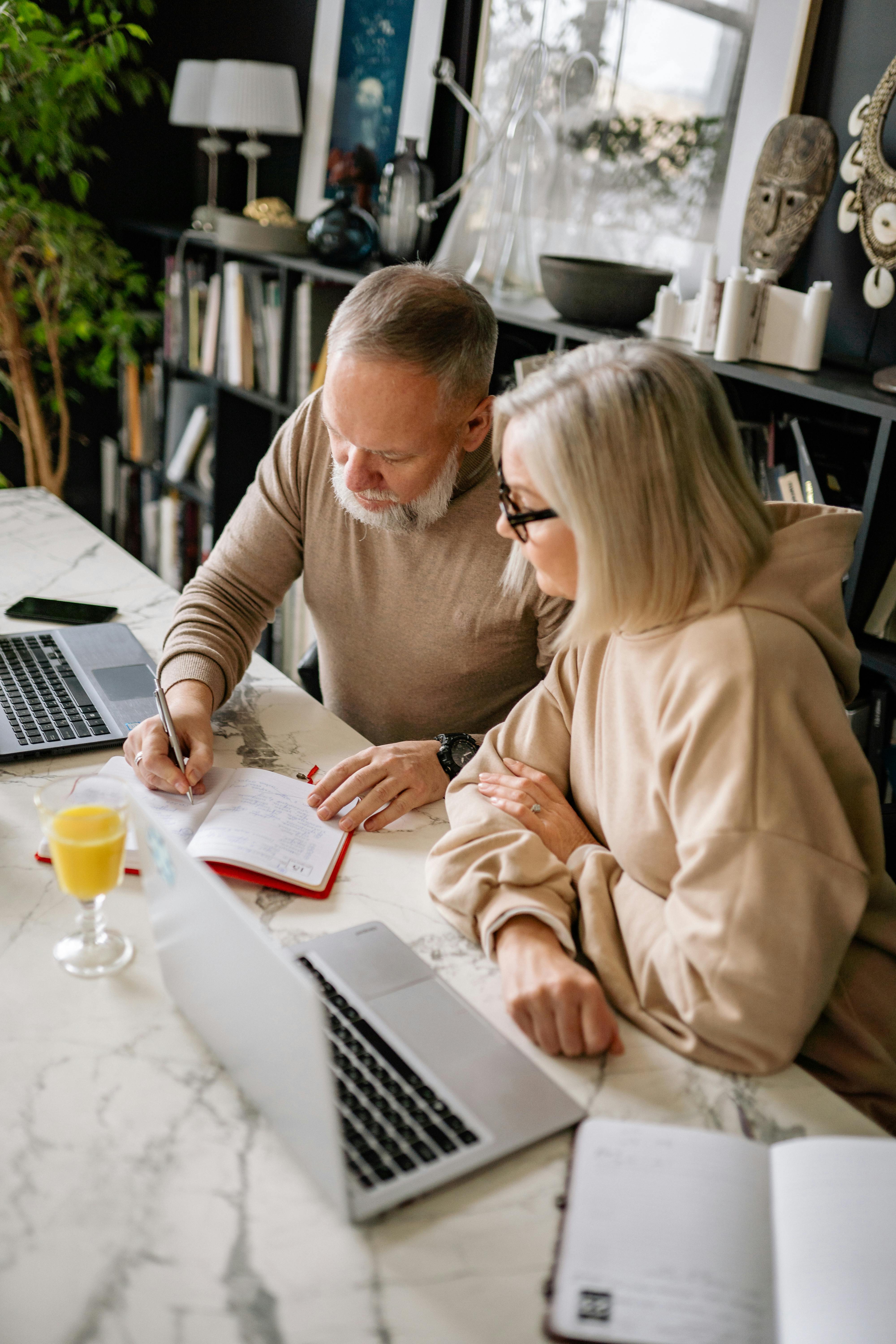 Middle-aged man and woman working together at a table with laptops and notebooks.