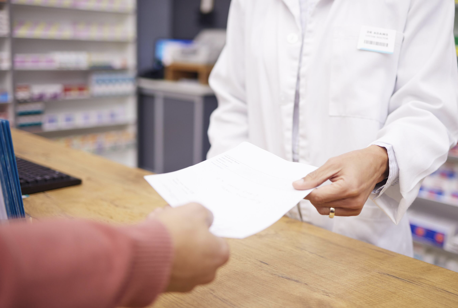 Pharmacist handing a prescription paper to a customer at the pharmacy counter