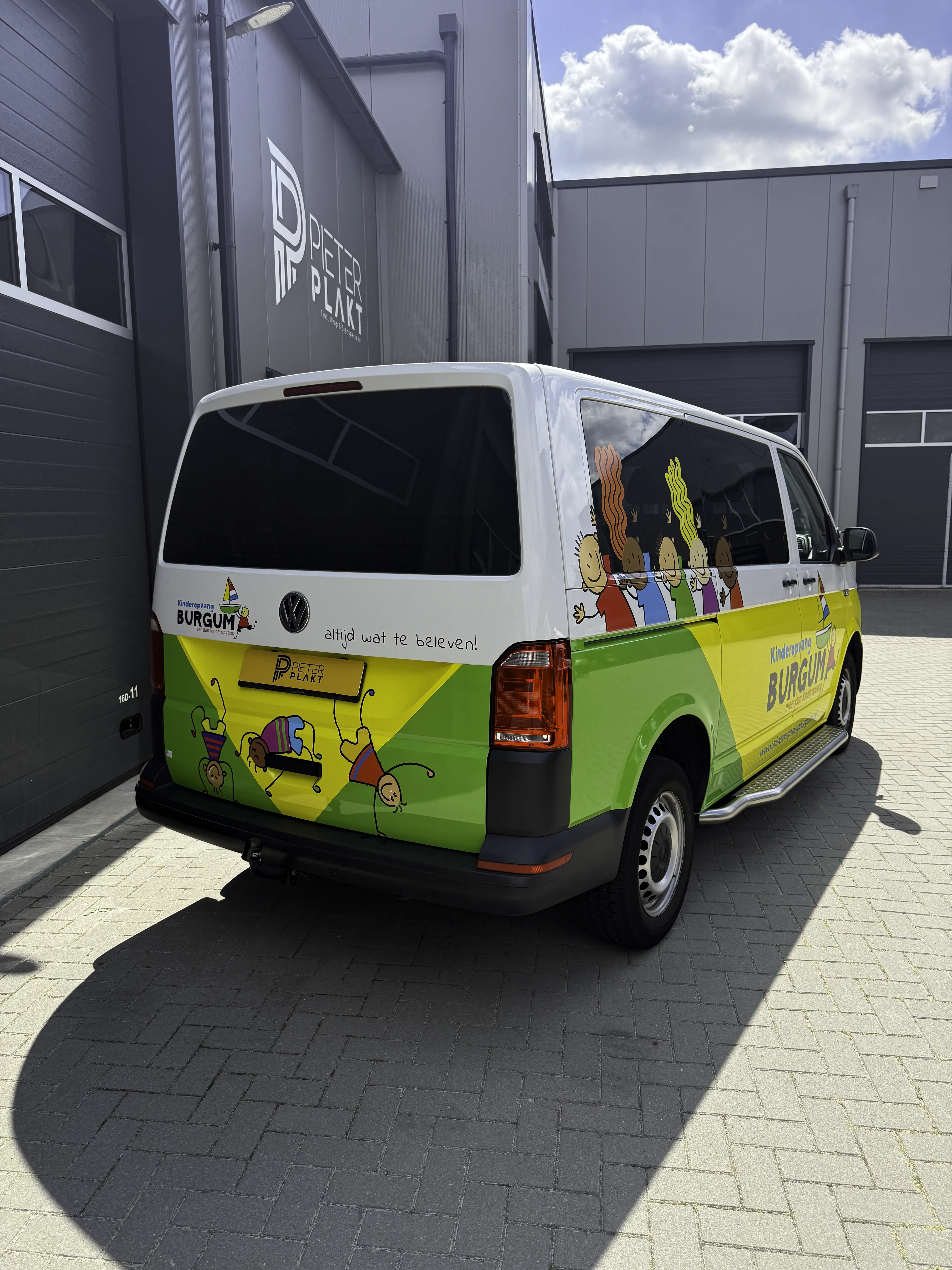 Achterzijde van de beletterde Volkswagen Transporter van Kinderopvang Burgum met belettering op de achterdeuren