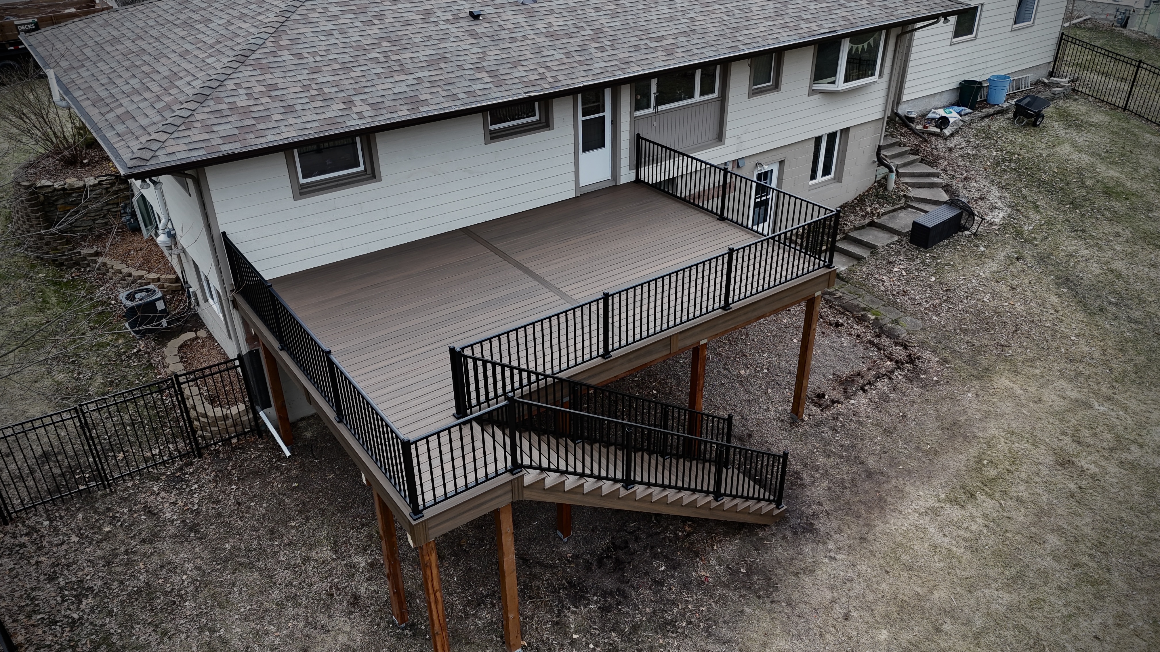 Raised wooden deck attached to a house with black metal railings and stairs leading to the ground.