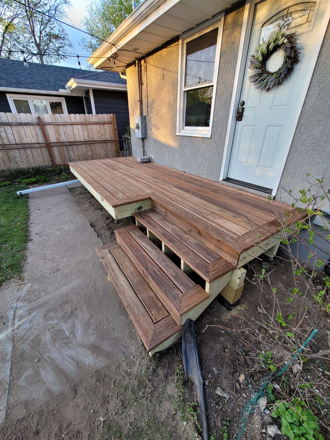Newly built wooden porch with three steps leading to a white door decorated with a wreath.