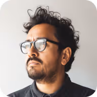 Man with glasses and curly hair looking to the side against a plain background.