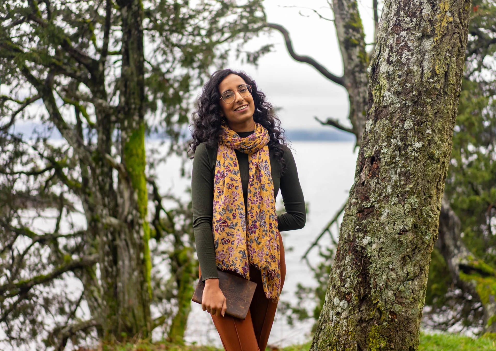 Priya standing among trees beside the water