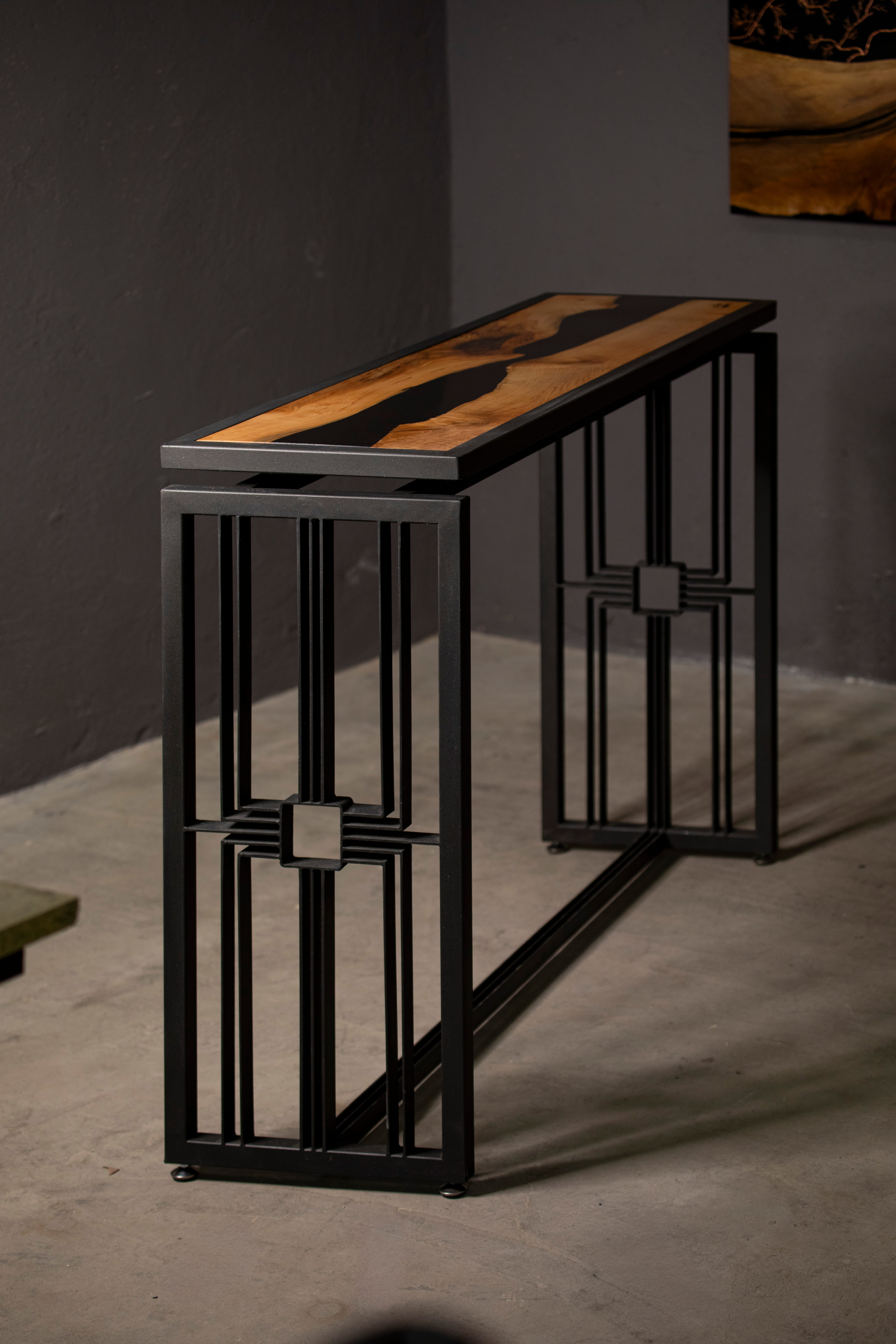 Table étroite avec plateau en bois clair et noir intégré, soutenue par une structure métallique noire géométrique.