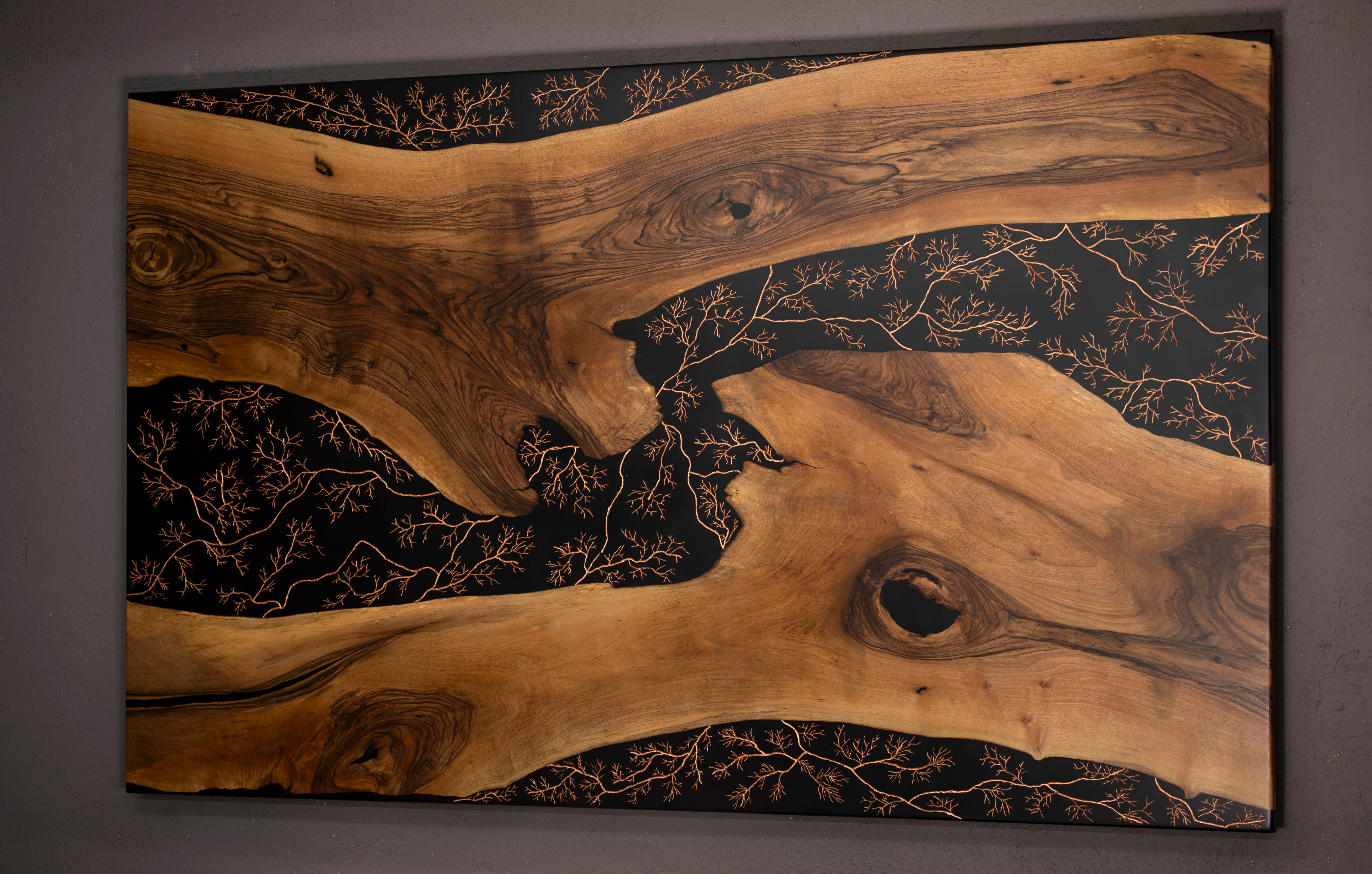 Table en bois avec motifs de branches conductrices en cuivre sur fond noir.