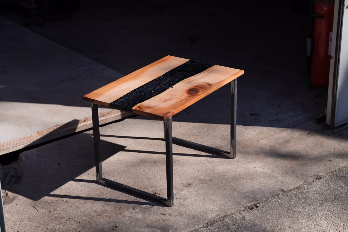 Table basse avec plateau en bois naturel clair à nervures et centre noir texturé, sur pieds métalliques carrés.