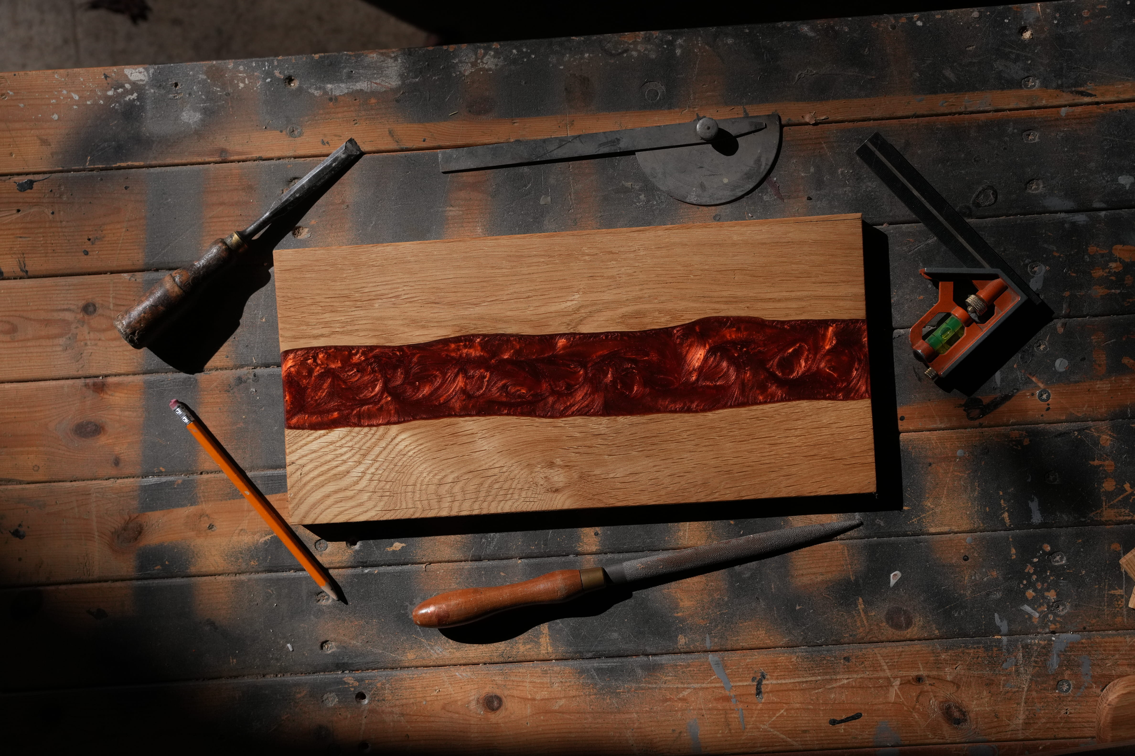 Planche de bois décorative avec résine rouge au centre, entourée d'outils de menuiserie sur une table.