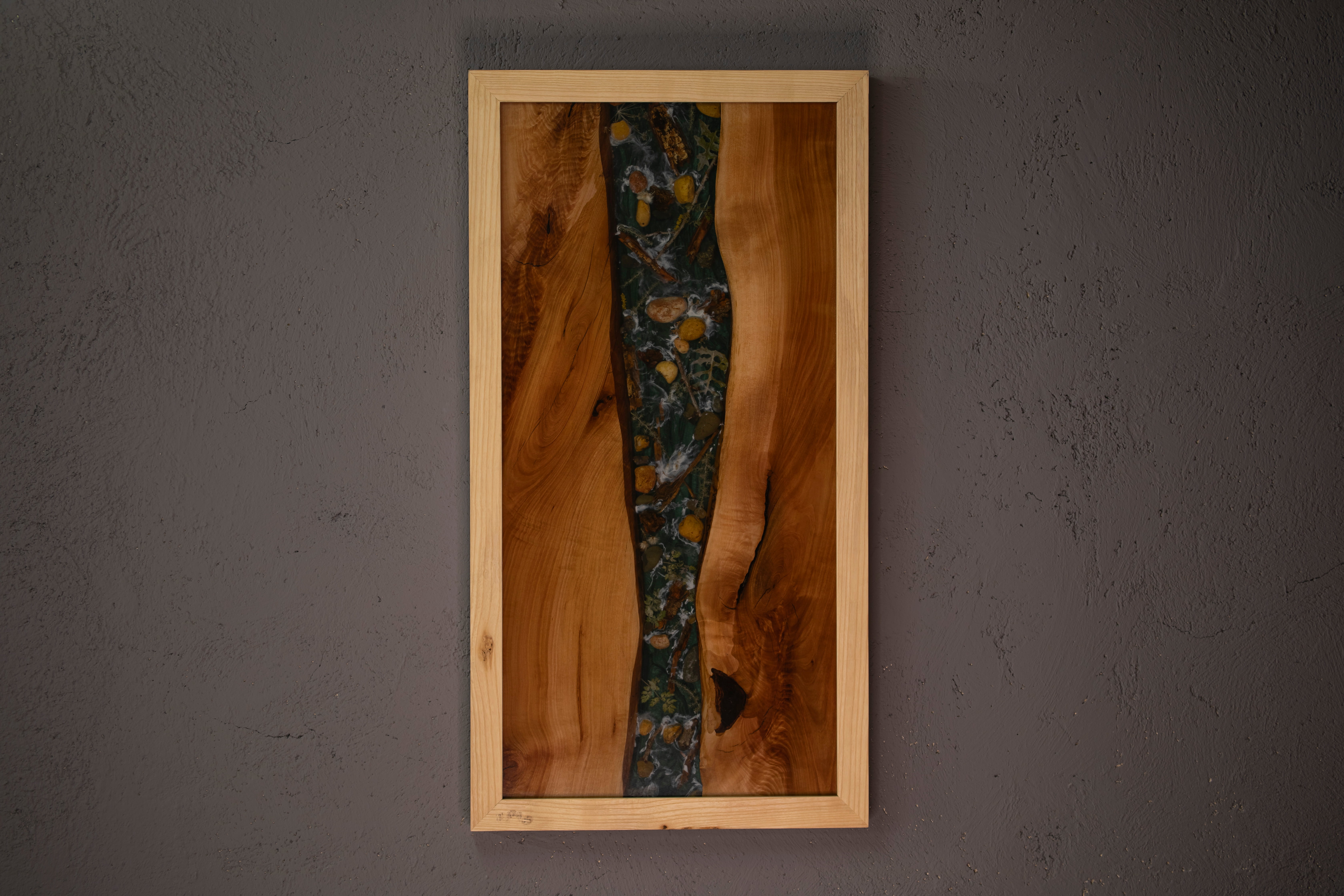Tableau mural en bois naturel avec une bande centrale en résine contenant des feuilles et pierres encastrées.