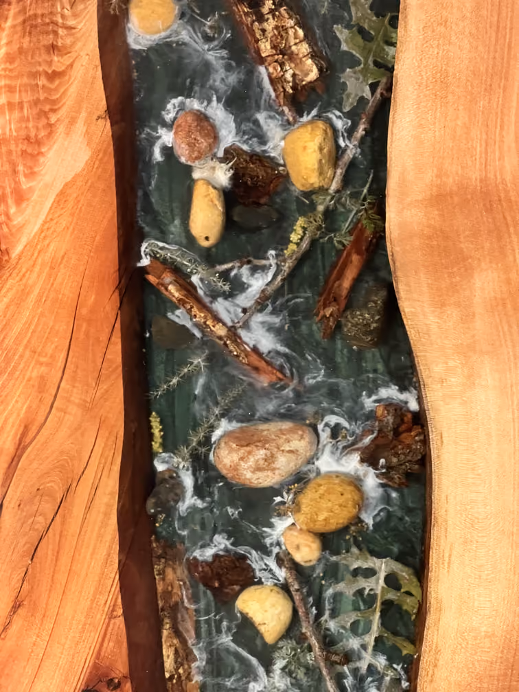 Plan rapproché d'une table en bois avec une rivière décorative en résine intégrant des pierres, branches, feuilles et mousse.