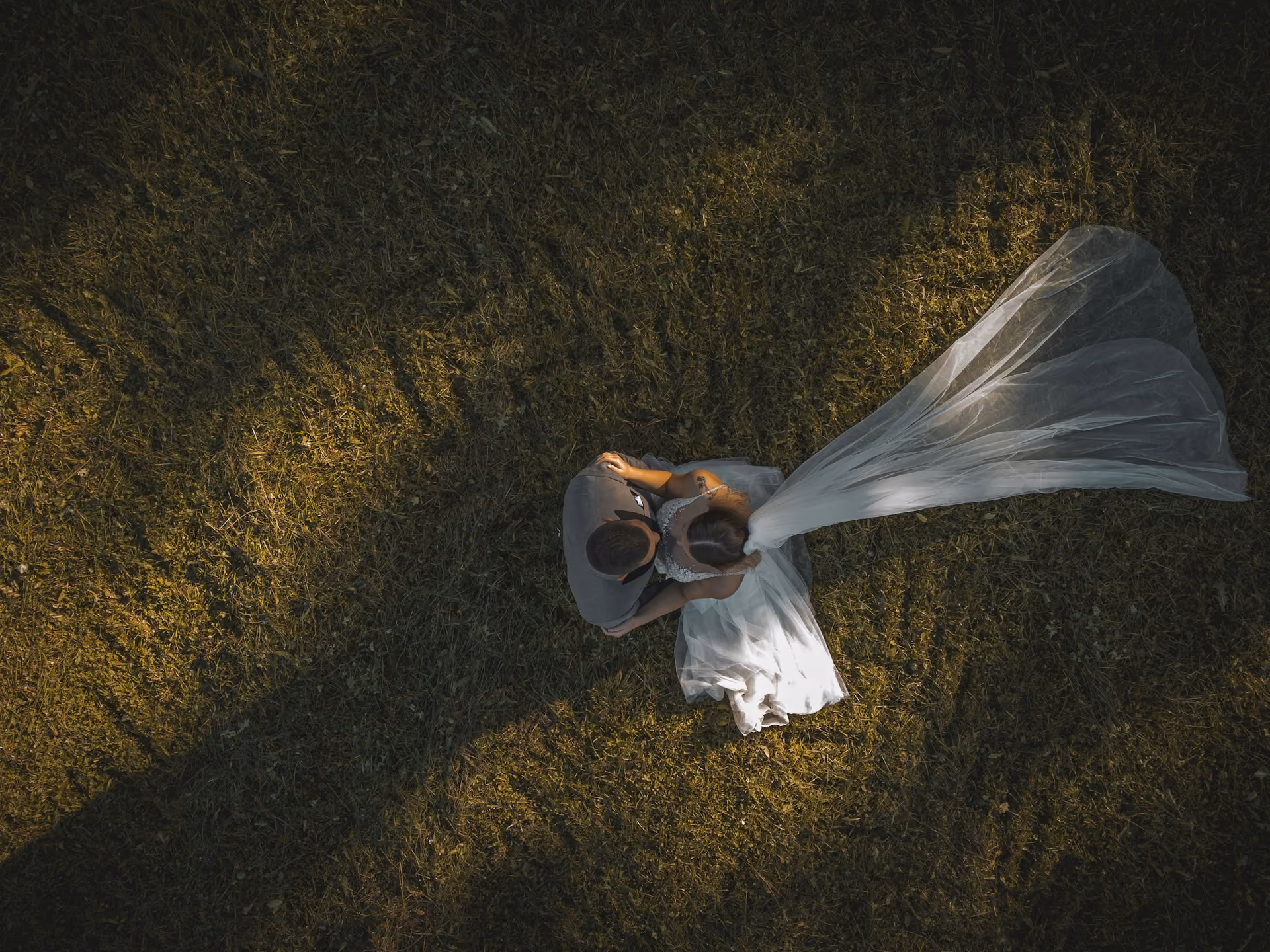 Vue aérienne d'un couple de mariés assis sur l'herbe, la mariée porte une robe blanche et un voile long.