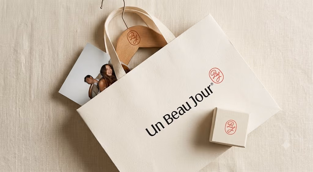 Un sac en toile blanc avec texte Un Beau Jour et un cintre en bois avec logo UBJ.