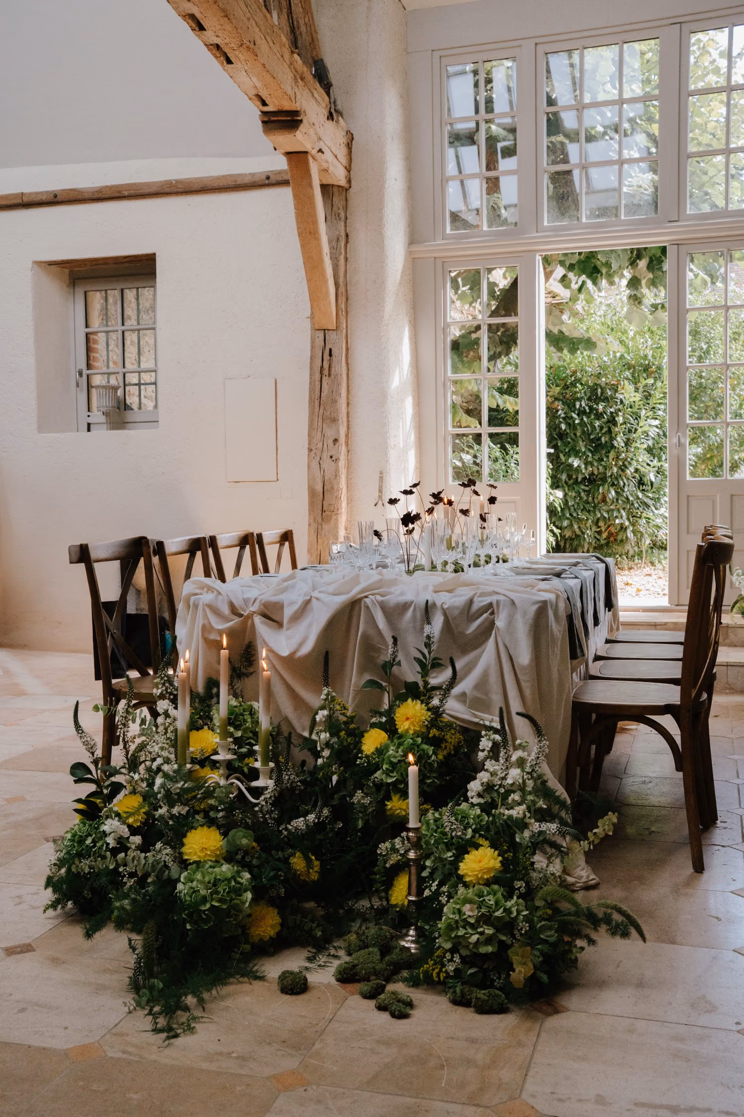 Table dressée avec des bougies allumées et des fleurs jaunes dans une salle lumineuse rustique.