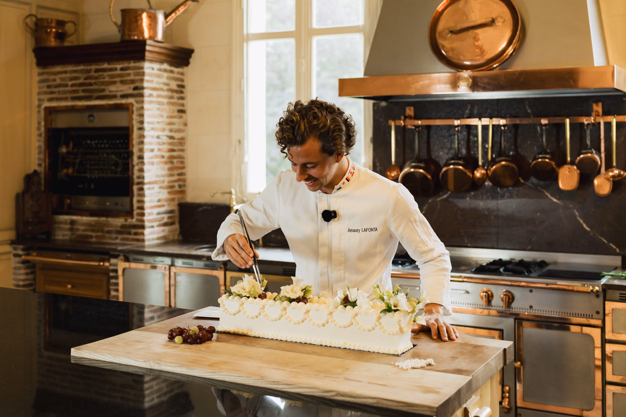 Un chef en cuisine orné d'un grand gâteau décoré de fleurs blanches, avec une atmosphère raffinée et élégante.