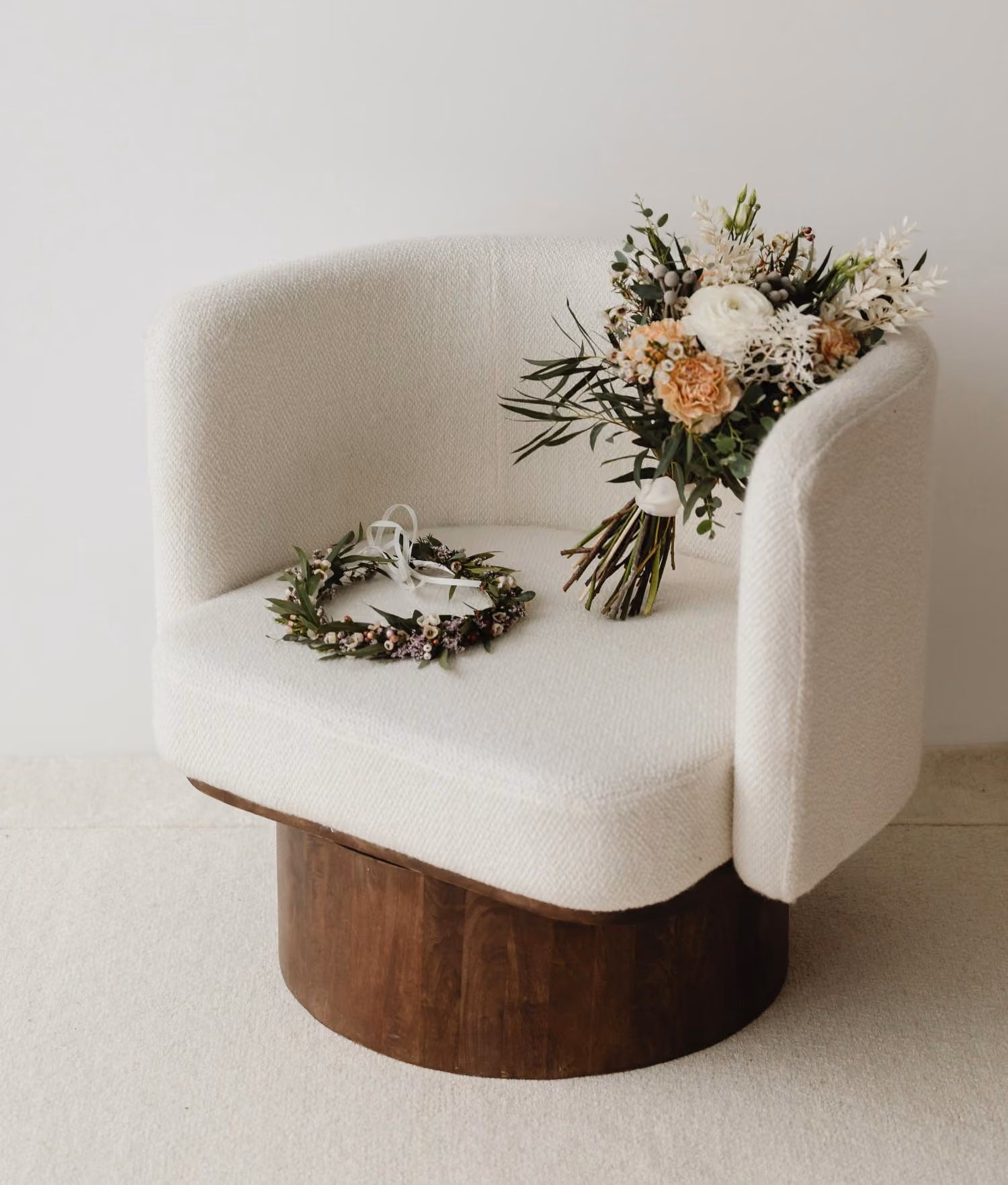 Un salon chaleureux avec un fauteuil blanc et une base en bois accueillant une couronne de fleurs et un bouquet de