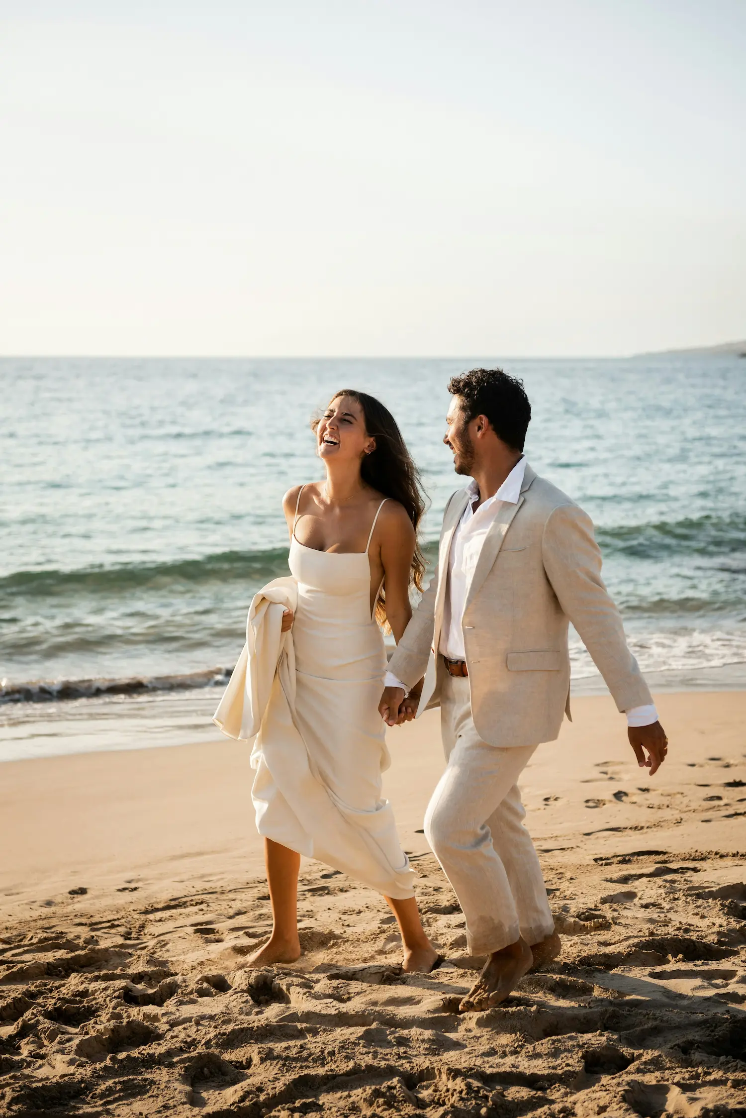 Une jeune mariée et son mari savourant un moment de bonheur sur la plage, vêtus de robes blanches élégantes contre un