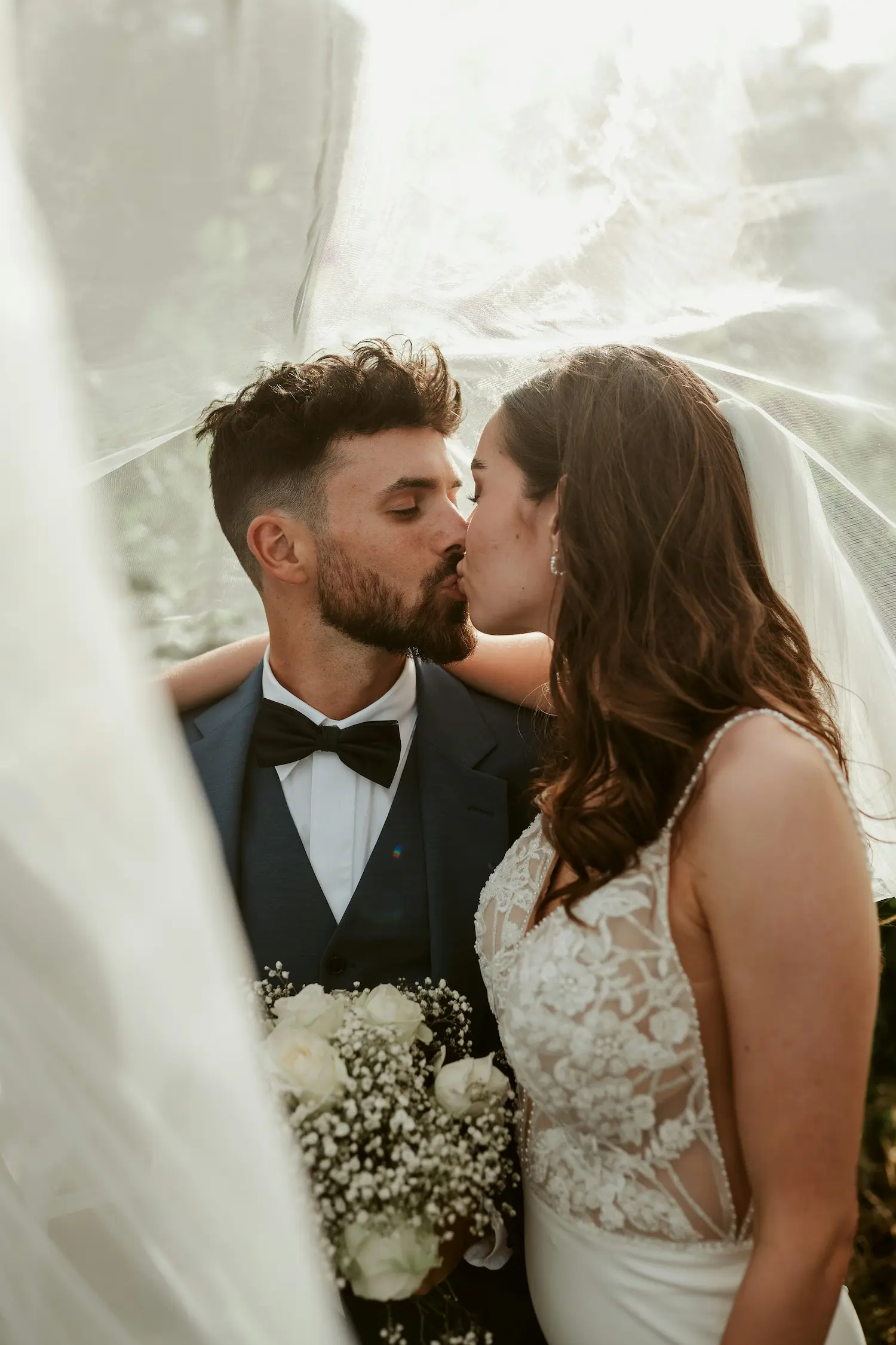 Un couple romantique partage un baiser tendre sous un voile de dentelle, incarnant l'élégance et la tendresse du mariage.