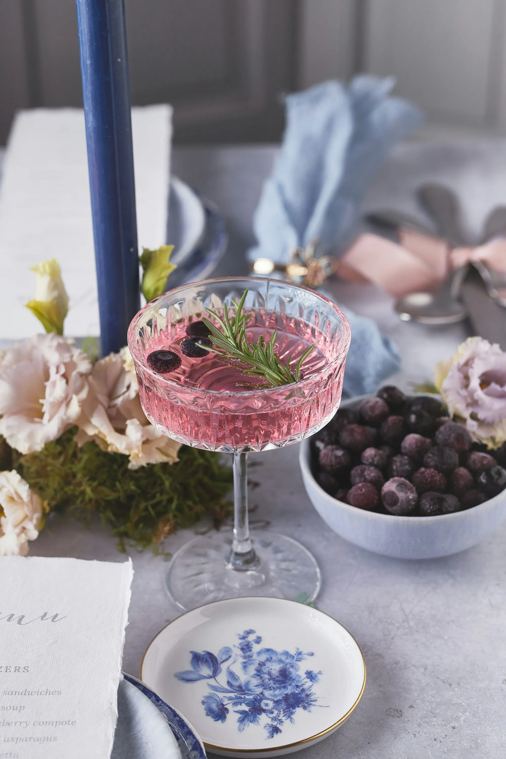 Un verre de champagne rose garni de fraises et de myrtilles, entouré de fleurs et de fruits frais, suggère un banquet